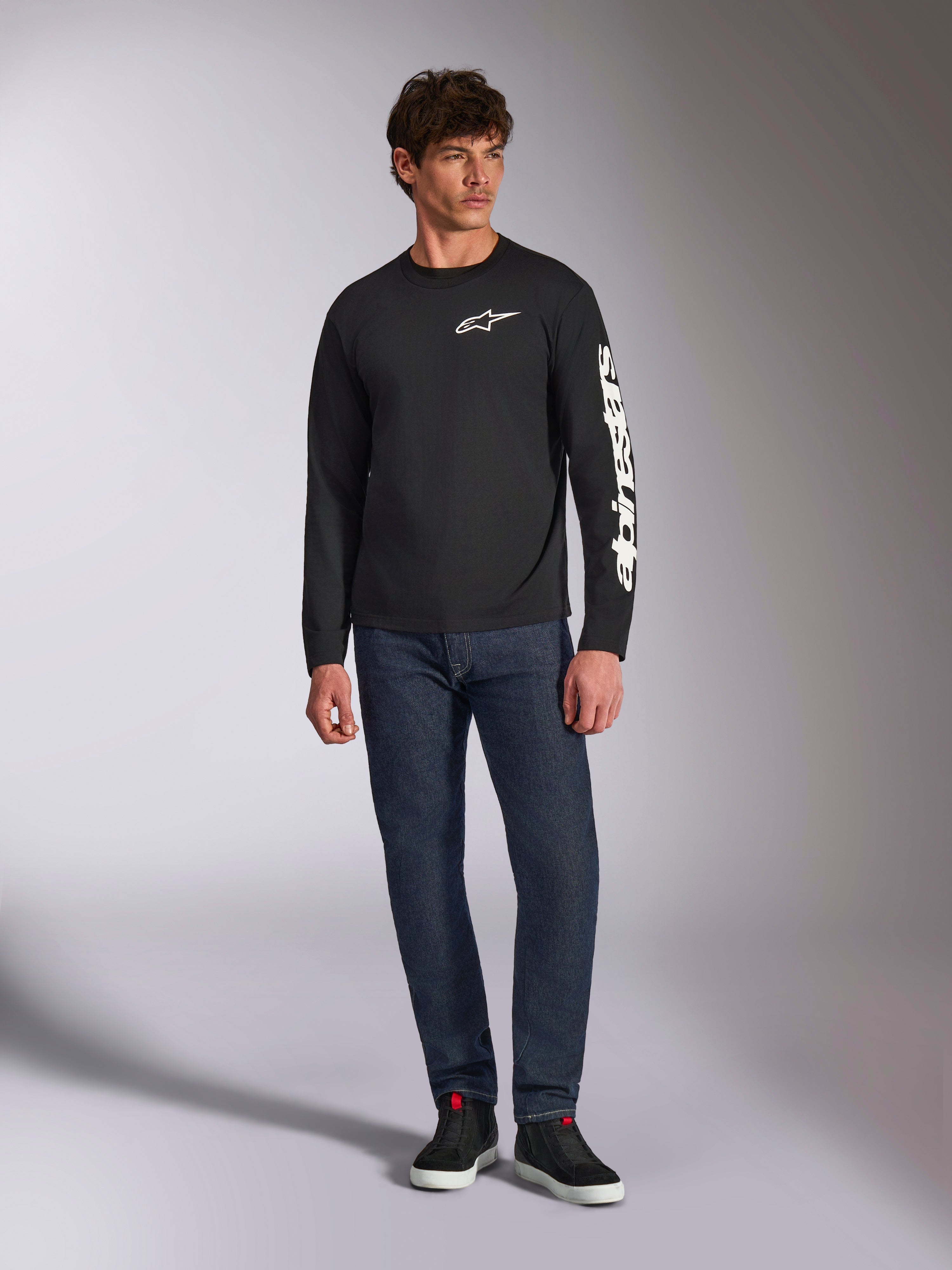 Alpinestars Trackside CSF Tee, långärmad t-shirt, svart och vit, bärs med mörkblå jeans och svarta sneakers, med vit Ride 4.0-logotyp på bröstet och Alpinestars ordmärke på ärmen, motorsportinspirerat streetwear