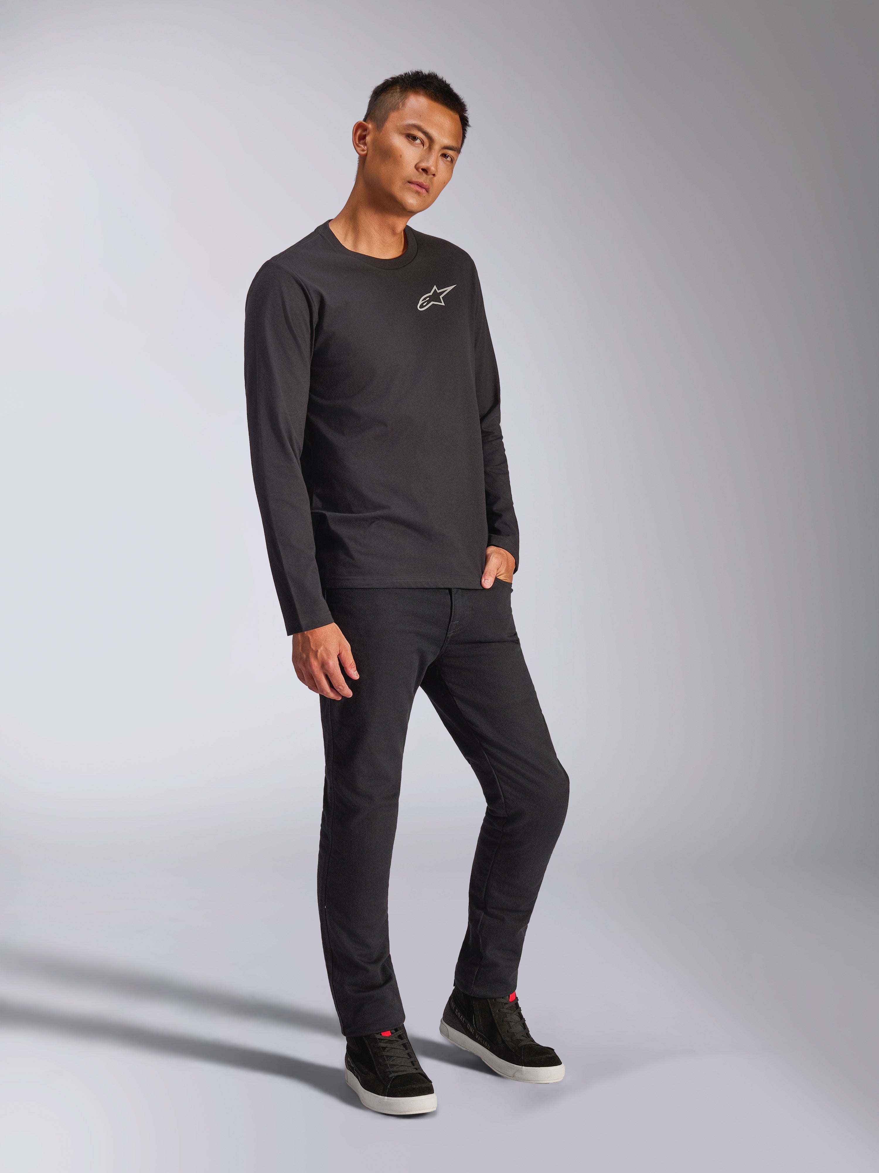 Alpinestars Trackside CSF Tee, långärmad t-shirt, svart, vit Astars-logotyp på bröstet, bärs av modell med svarta byxor och sneakers, avslappnad motorsportinspirerad streetwear