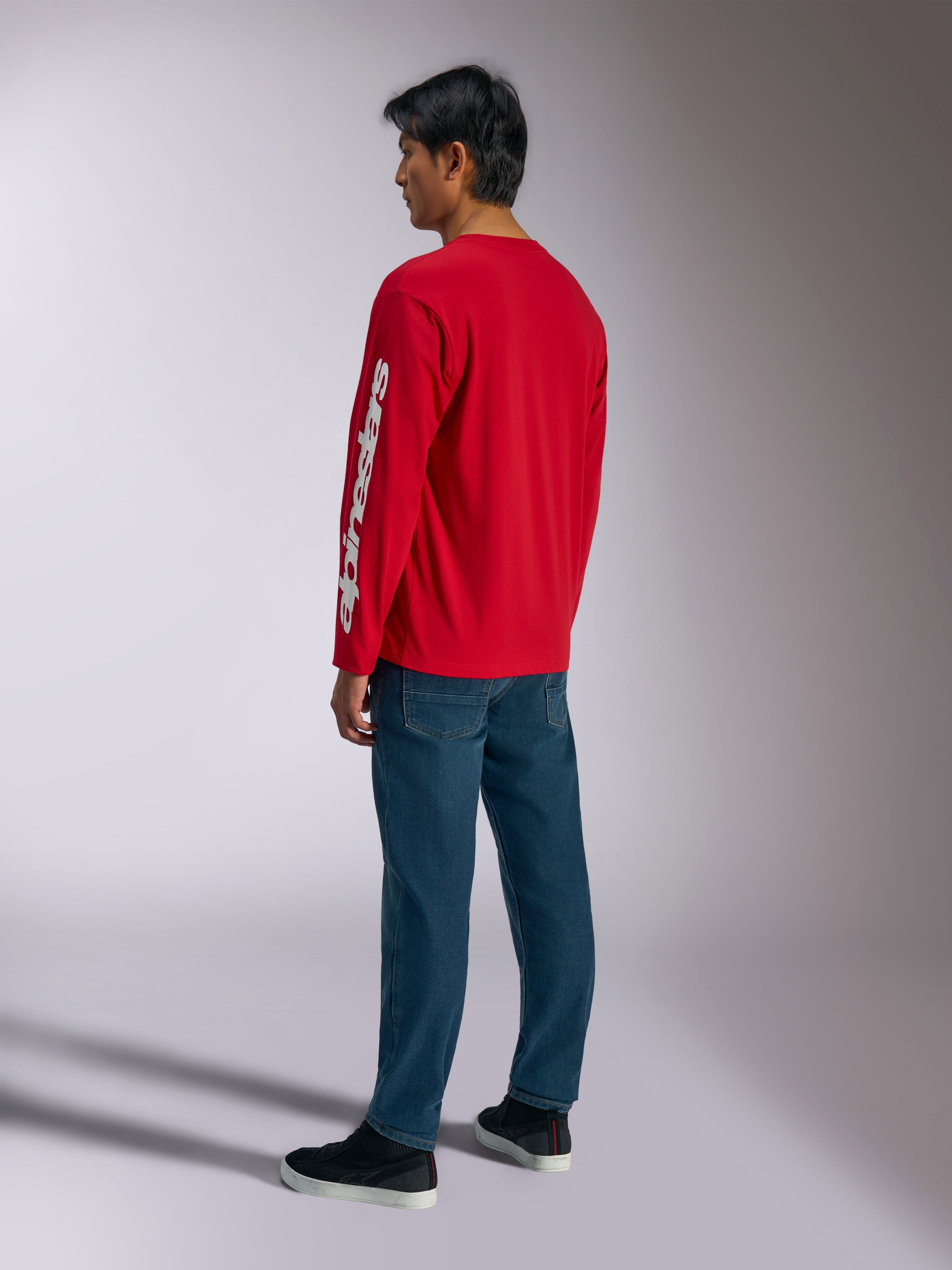 Alpinestars Trackside CSF Tee, långärmad t-shirt, röd, med en vit vertikal Alpinestars-logotyp på ärmen, bärs av en modell med blå jeans och svarta sneakers, avslappnat motorsportinspirerat streetwear