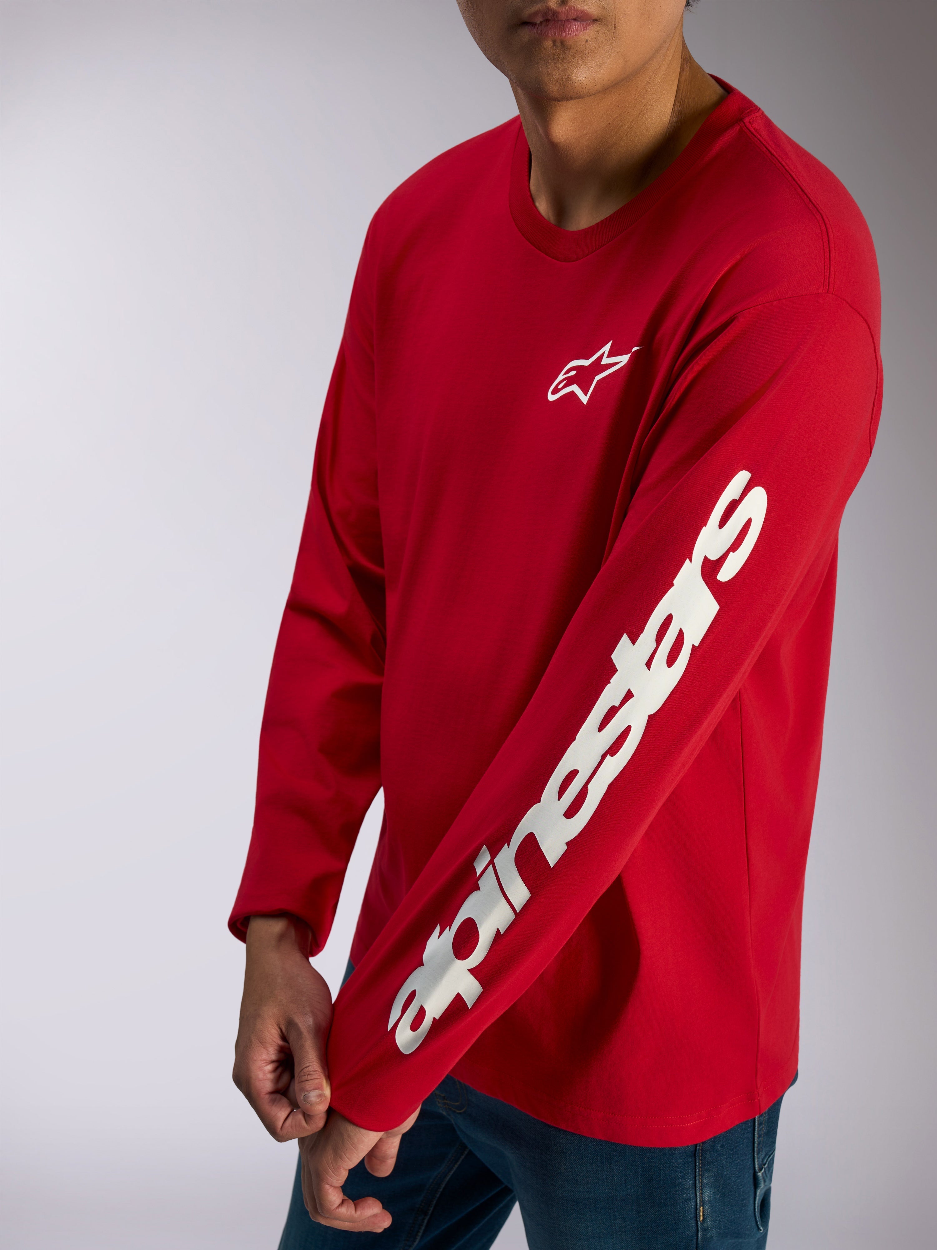 Alpinestars Trackside CSF Tee, långärmad t-shirt, röd, vit Alpinestars-logotyp på bröstet och ett tydligt ordmärke på ärmen, casual motorsport-streetwear buren med blå jeans