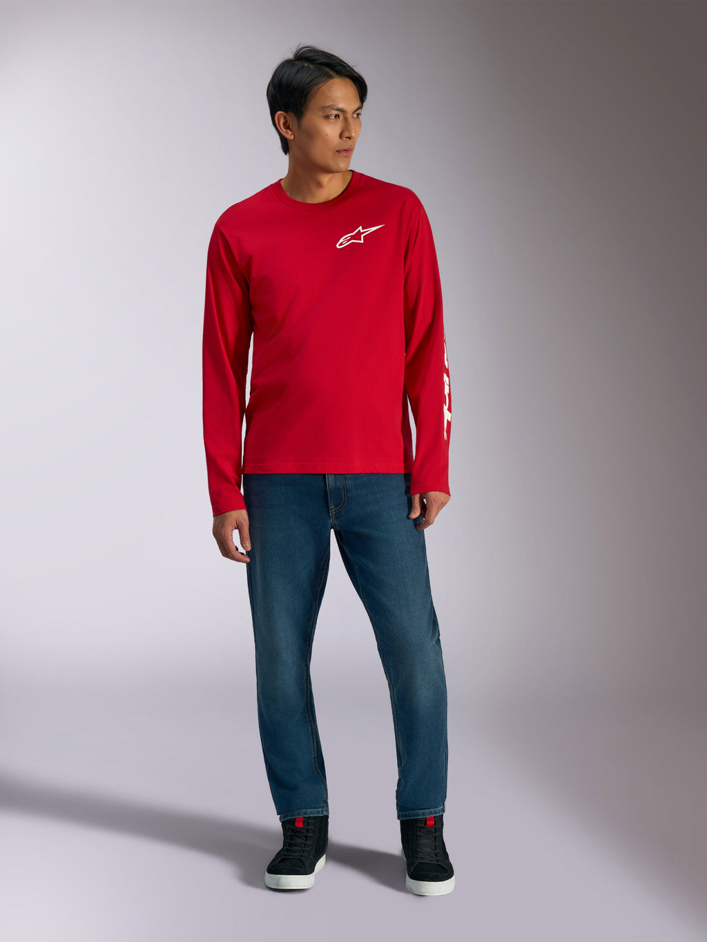 Alpinestars Trackside CSF Tee, långärmad t-shirt, röd med vit Alpinestars-logotyp, lifestyle-bild buren med blå jeans och svarta sneakers, avslappnade motorsportinspirerade sportkläder