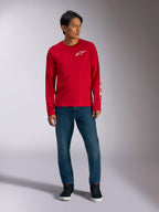 Alpinestars Trackside CSF Tee, långärmad t-shirt, röd med vit Alpinestars-logotyp, lifestyle-bild buren med blå jeans och svarta sneakers, avslappnade motorsportinspirerade sportkläder