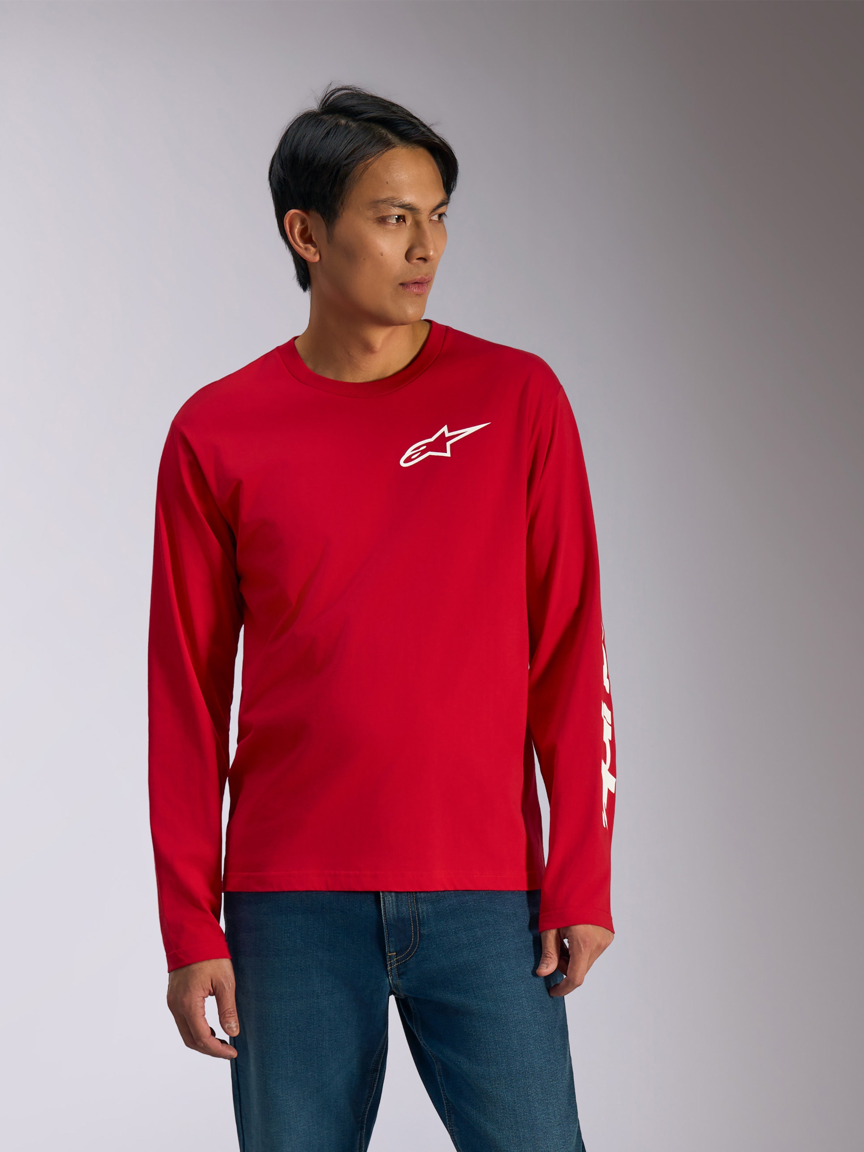 Alpinestars Trackside CSF Tee, långärmad t-shirt, röd med vit grafik, vit Alpinestars-stjärnlogotyp på bröstet och vit text på ärmen, bärs med blå jeans, vardagliga motorsport-inspirerade sportkläder