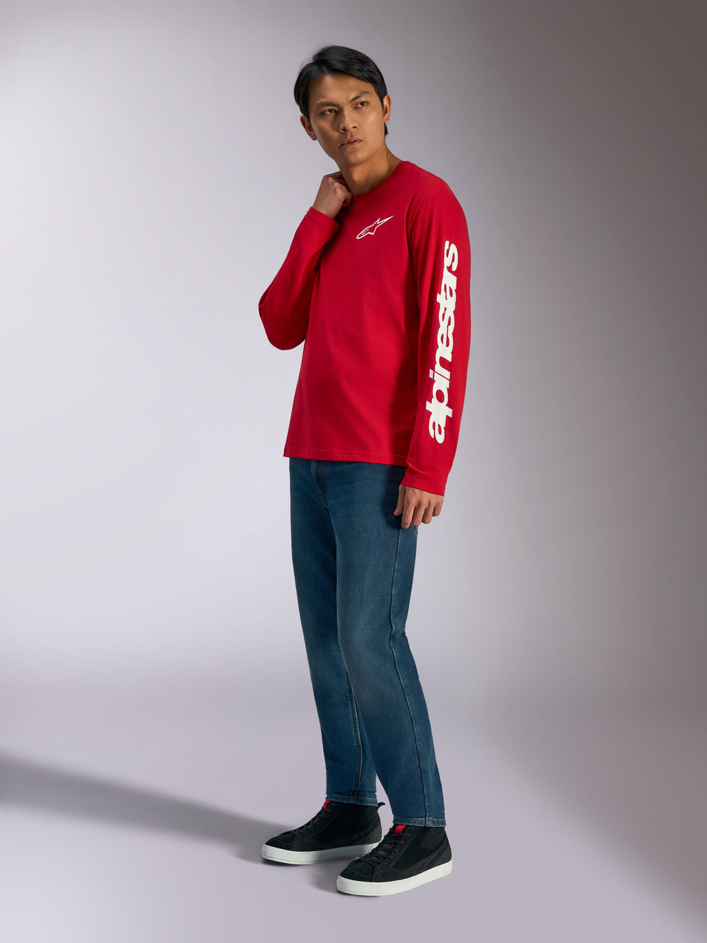 Alpinestars Trackside CSF långärmad t-shirt, röd med vit Alpinestars-logotyp på bröstet och ärmen, bärs av modell med blå jeans och svarta sneakers, avslappnat motorsport-inspirerat streetwear