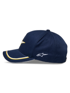 Alpinestars Ascension Snapback keps, marinblå och guld, sidoprofil med en böjd skärm med dubbel soutache-kant i guld och vitt, broderad sidologotyp, avslappnad motorsport-streetwear