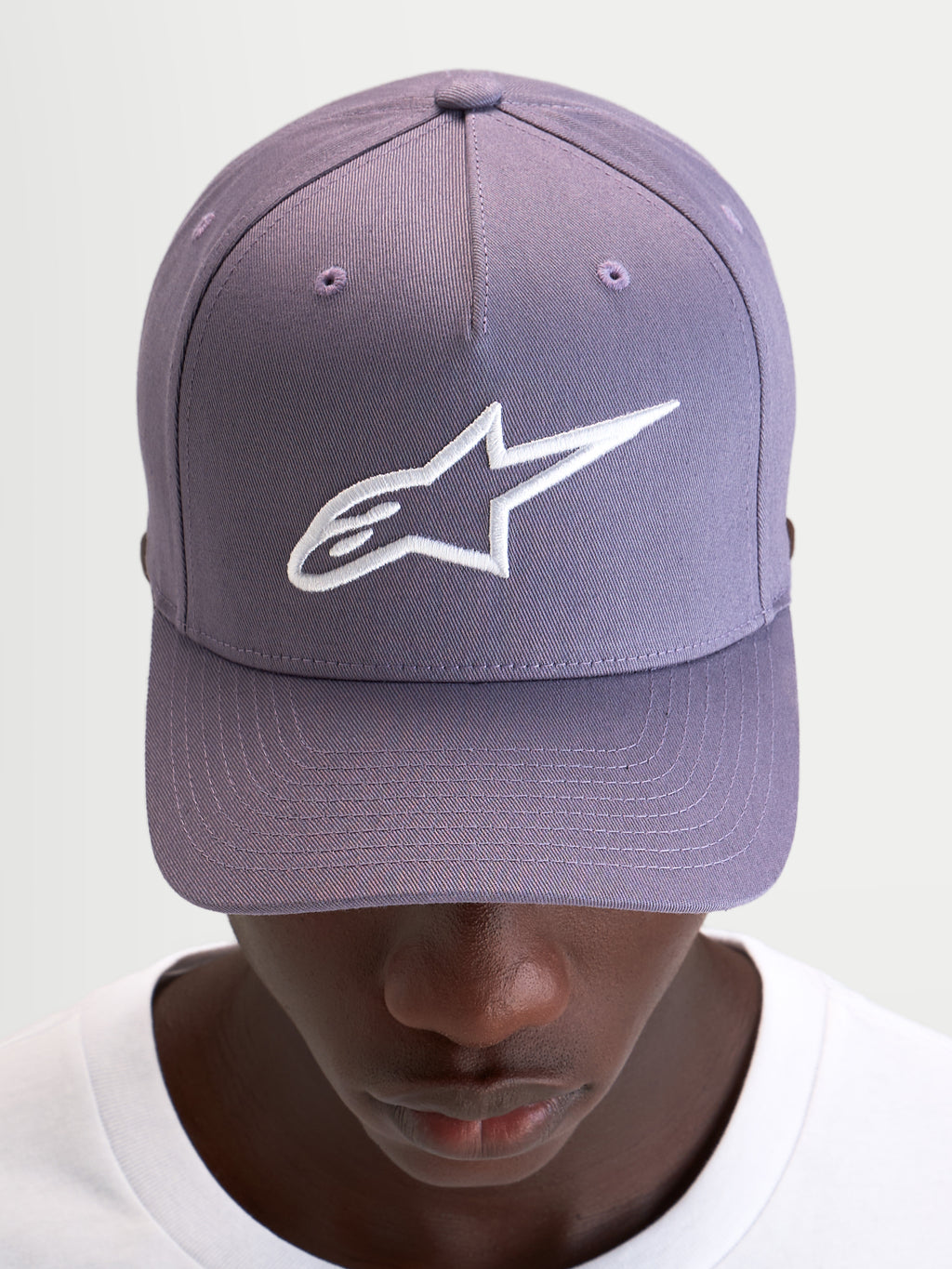 Alpinestars Ageless Snapback keps, lila sportswear-keps med böjd skärm, strukturerad krona och vit broderad Astars-logotyp på framsidan, bärs av en modell