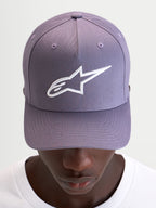 Alpinestars Ageless Snapback keps, lila sportswear-keps med böjd skärm, strukturerad krona och vit broderad Astars-logotyp på framsidan, bärs av en modell