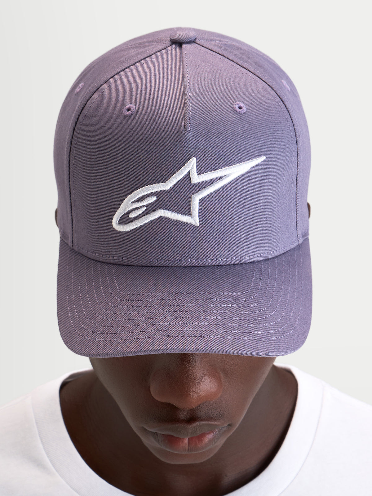 Alpinestars Ageless Snapback keps, lila sportswear-keps med böjd skärm, strukturerad krona och vit broderad Astars-logotyp på framsidan, bärs av en modell