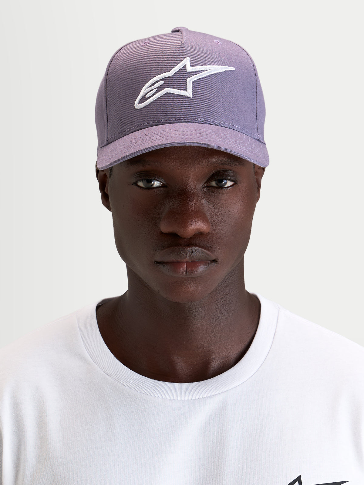 Alpinestars Ageless Snapback keps, lila och vit keps med böjd skärm och strukturerad twillprofil, bärs av en modell som visar den broderade Astars-logotypen framtill