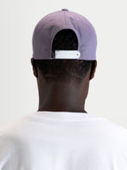 Alpinestars Ageless Snapback keps, lila och vit, vy bakifrån som visar den justerbara vita snapback-stängningen och den strukturerade kronan, bärs av en modell