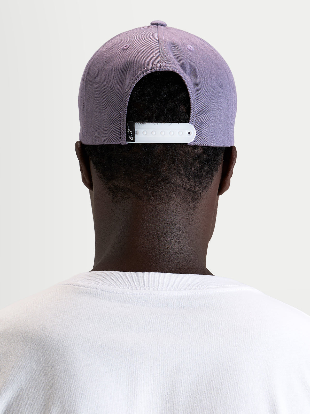 Alpinestars Ageless Snapback keps, lila och vit, vy bakifrån som visar den justerbara vita snapback-stängningen och den strukturerade kronan, bärs av en modell