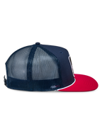 Alpinestars Control Trucker-keps, marinblå och röd, sidoprofil som visar framsida i marinblå twill och bakpaneler i mesh, platt röd skärm med vit flätad snördetalj, vardaglig motorsportinspirerad huvudbonad