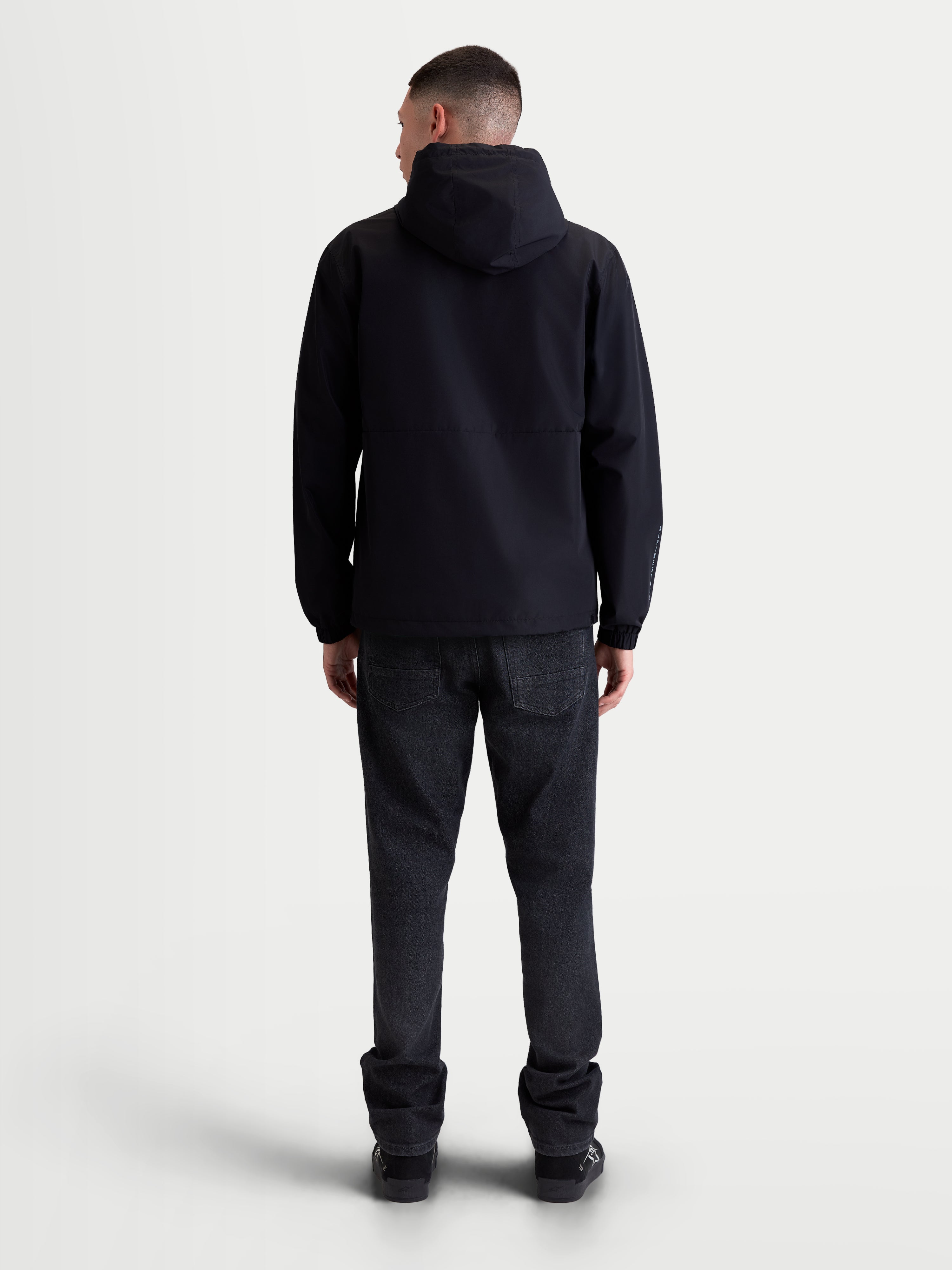Alpinestars Speeder Resolve jacka vindstopp, svart lättviktsjacka för urban användning, unisex-modell med huva sedd bakifrån, meshfodrad andningsbar konstruktion med justerbar huva och fåll.