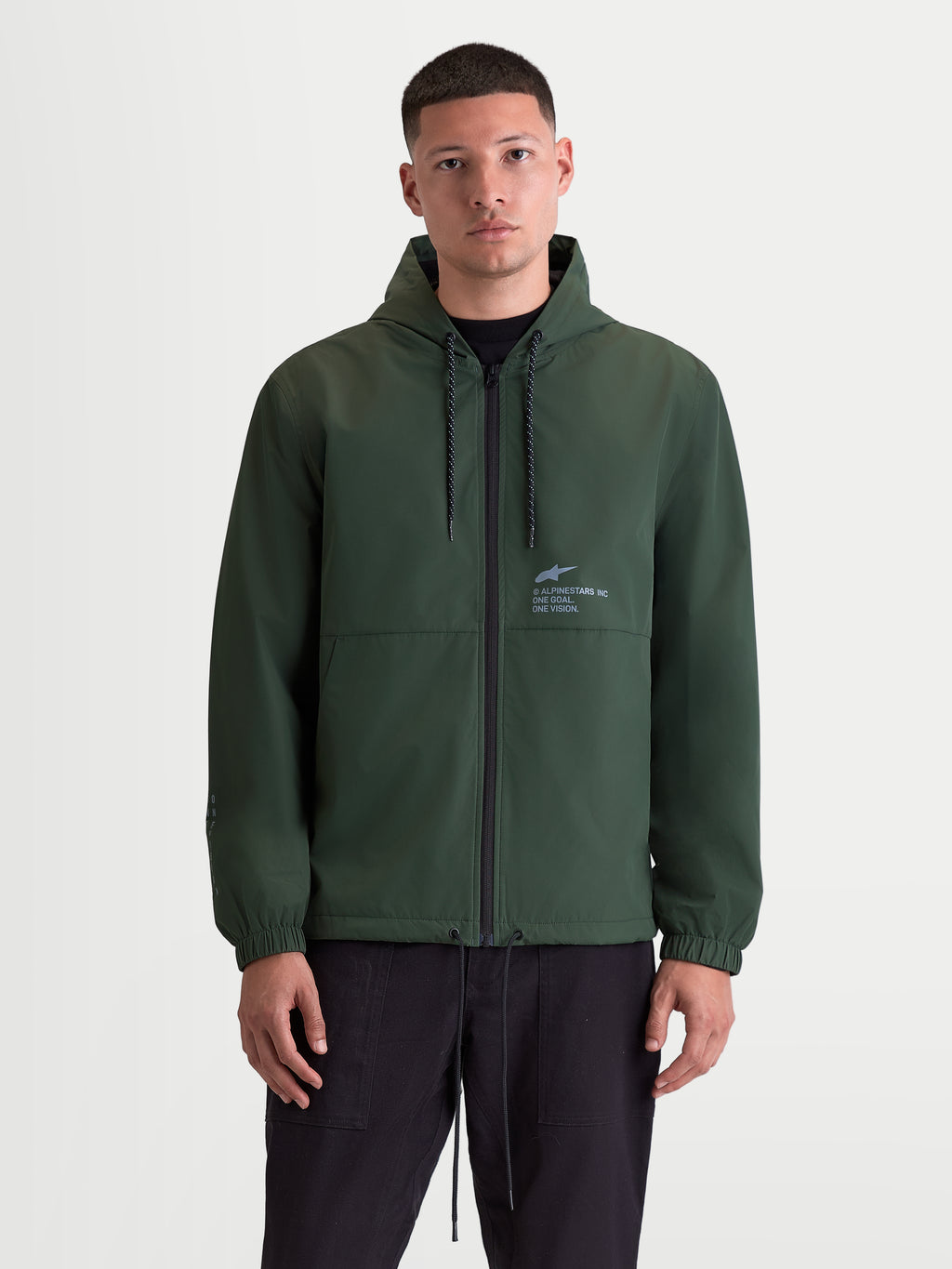 Alpinestars Speeder Resolve vindstoppsjacka, lättviktssportwear för urban användning, grön jacka med huva för herrar, meshfodrad interiör, justerbar dragskohuva, hel dragkedja fram och Alpinestars logotyp på bröstet, framifrån på modell.