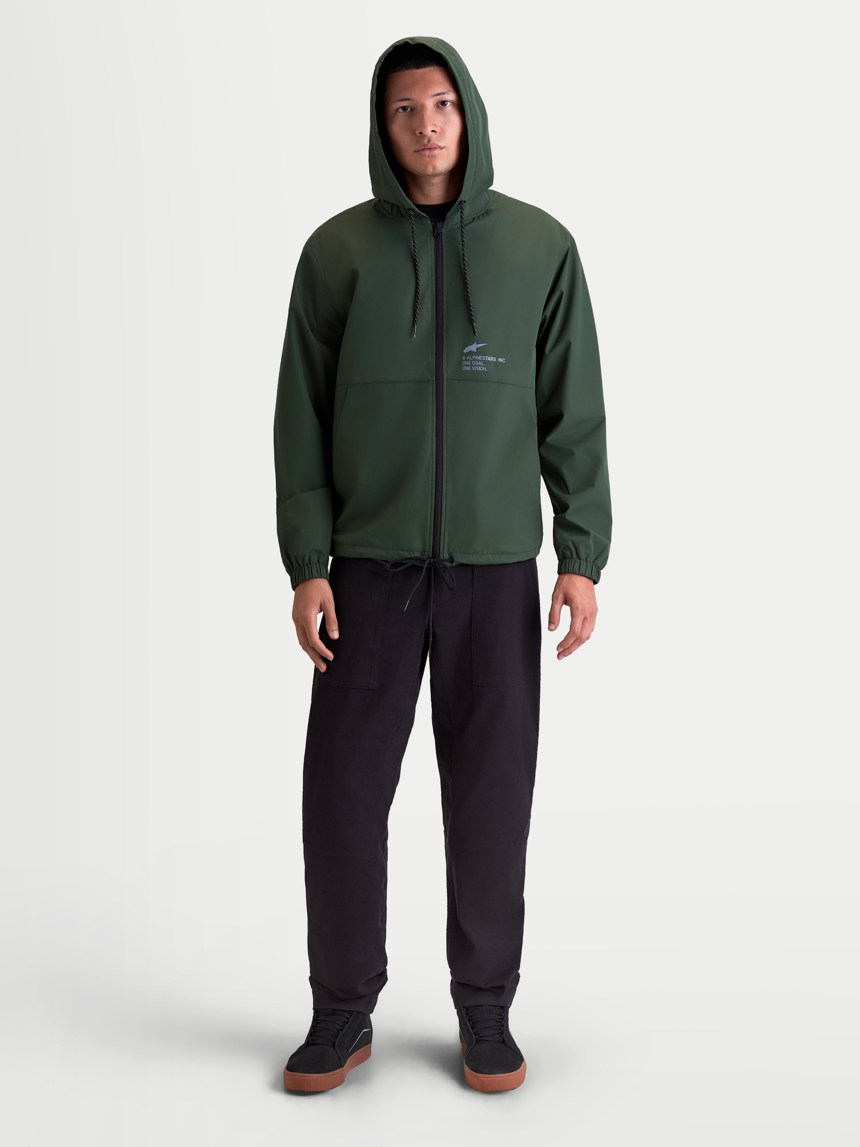 Alpinestars Speeder Resolve vindstopp-jacka, lätt sportswear-jacka för urban användning, grön, meshfodrad konstruktion med justerbar huva och omvänd spiraldragkedja, Alpinestars-branding på bröstet, frontvy på modell.