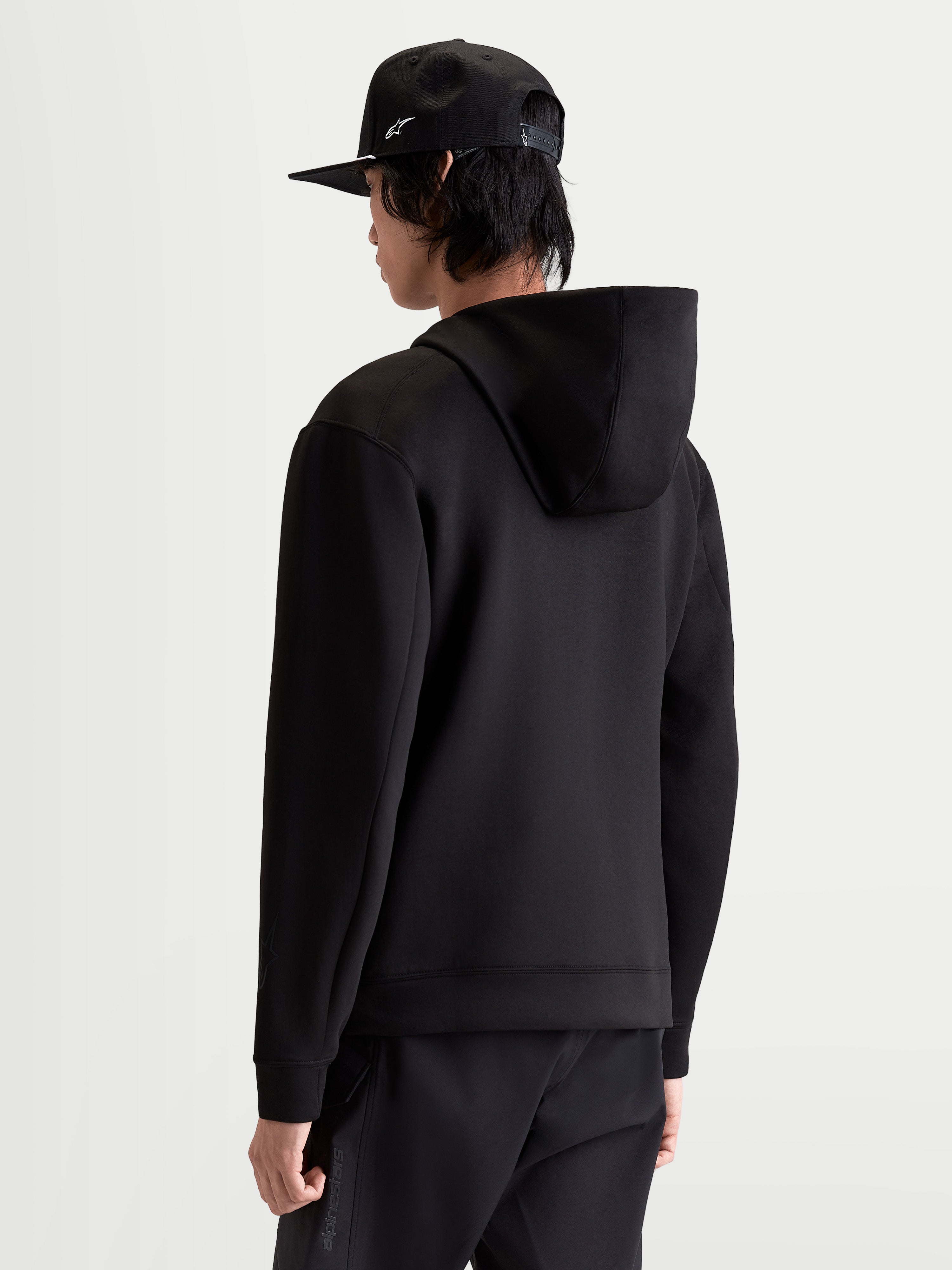 Alpinestars Datrix huvtröja, sportswearpullover för herr i svart, sedd bakifrån på modell. Visar den dubbelvävda fleecekonstruktionen och den meshfodrade huvan för vardagskomfort och en motorsportinspirerad stil.