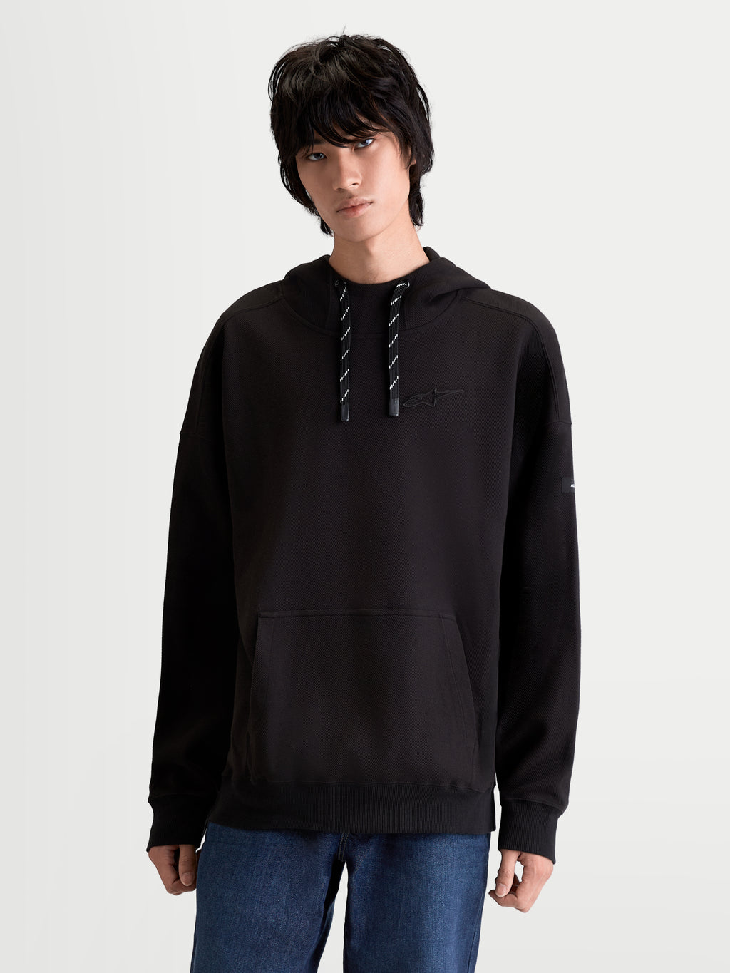 Alpinestars Camino Textured Oversized huvtröja, svart lifestyle-tröja i texturerad stickad twillfleece, hög krage, känguruficka och tonalt broderad logotyp på bröstet, manlig modell