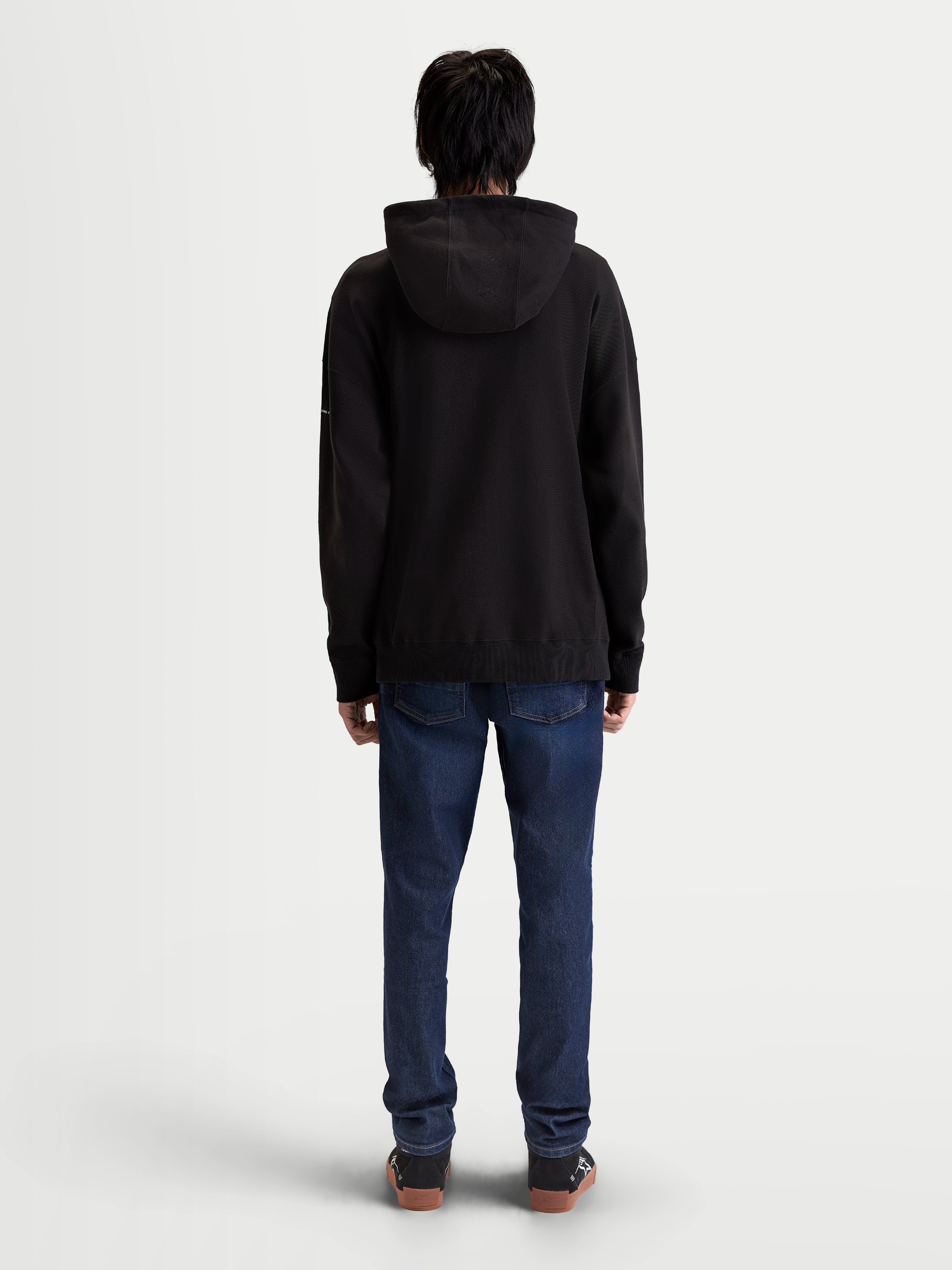 Alpinestars Camino Textured Oversized huvtröja, svart premiumhuvtröja i texturerad stickad twillfleece, sedd bakifrån på modell, avslappnad oversized passform, livsstilskläder.