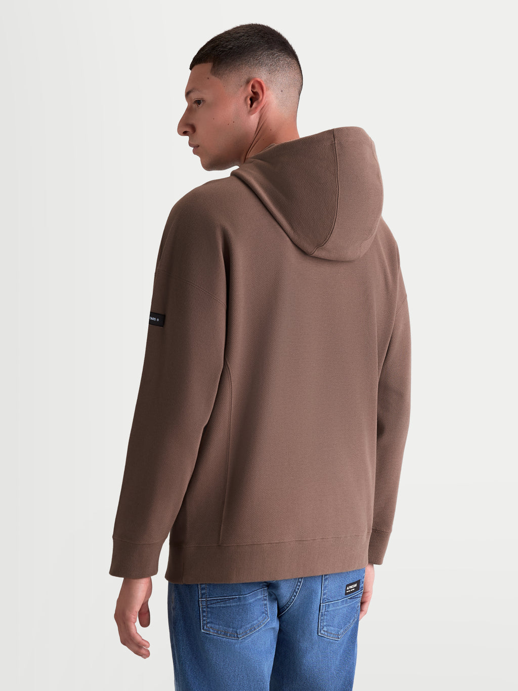 Alpinestars Camino Textured Oversized huvtröja, brun huvtröja i texturstickad twillfleece sedd bakifrån, avslappnad oversized passform med Alpinestars-märkning på ärmen, bekväm streetwear för vardagsbruk.