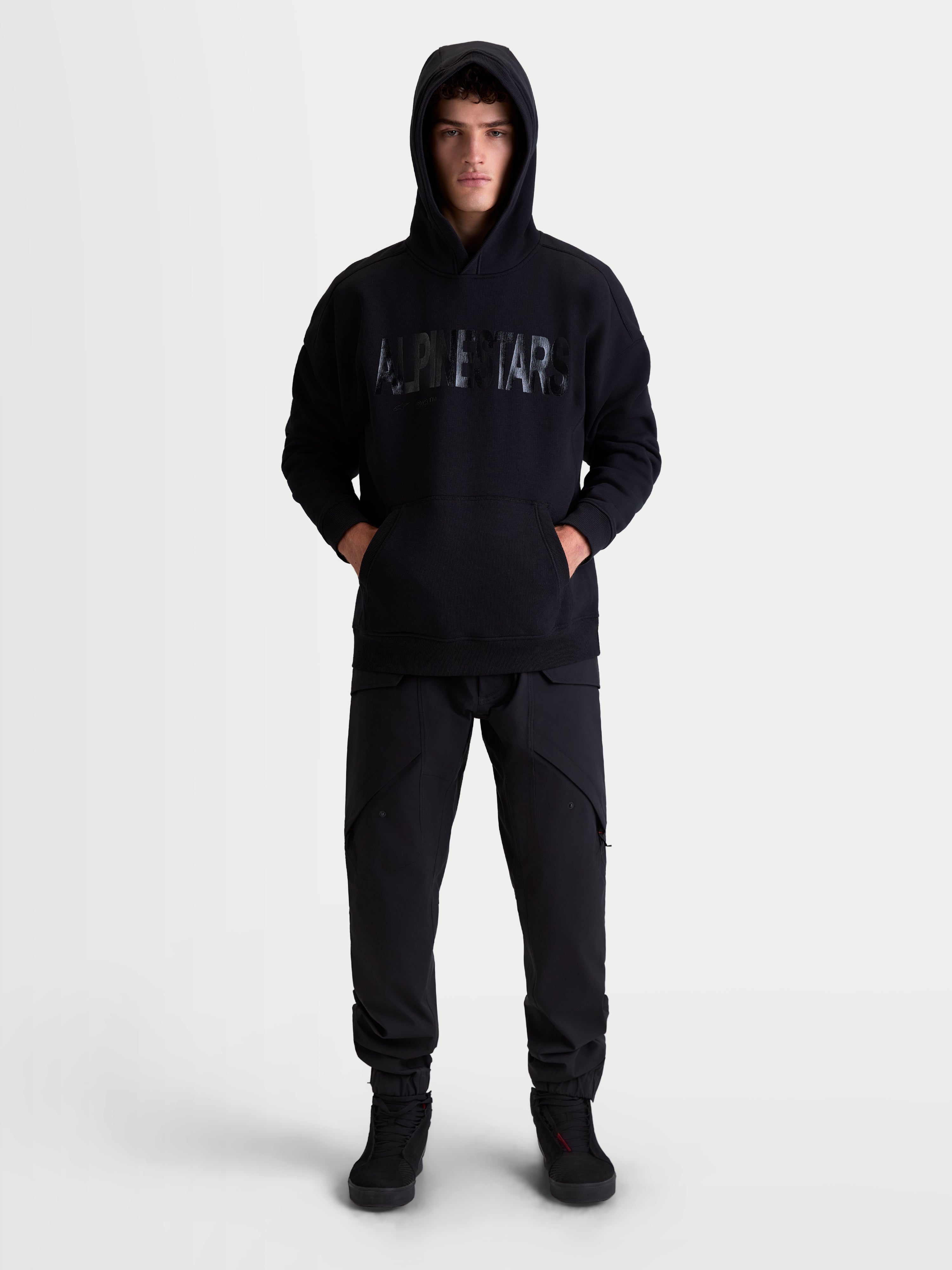 Alpinestars Shaw Oversized Hoodie, Men's and Women's Relaxed Sportswear Pullover, Black, featuring a textured front word logo, kangaroo pocket, and self-lined hood, premium cotton and recycled polyester fleece construction.