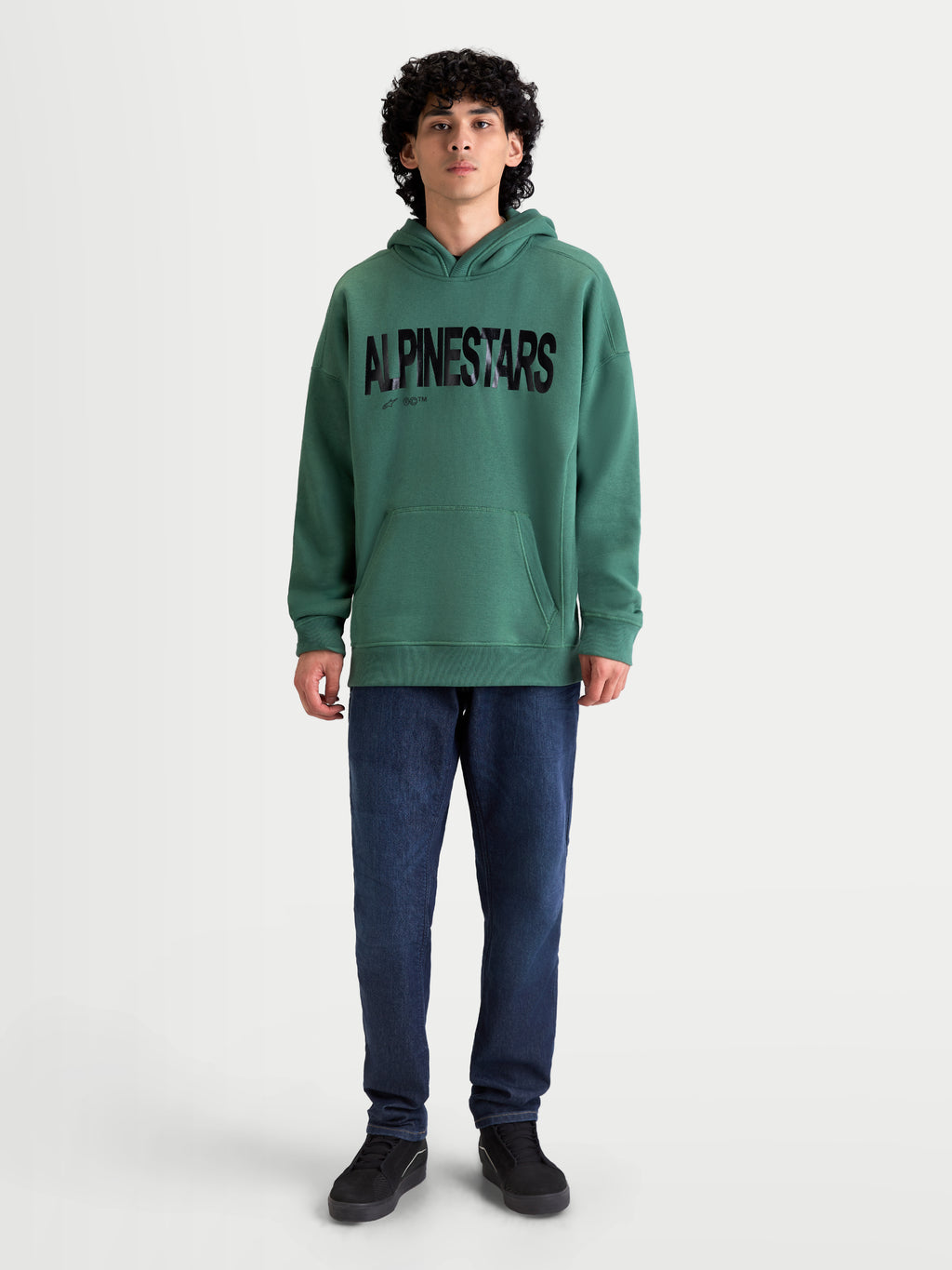 Alpinestars Shaw Oversized huvtröja, grön sportswear-huvtröja med svart texturerad logotyp framtill, oversized passform, blandning av bomull och återvunnen polyester, känguruficka och självfodrad huva, visas på modell.