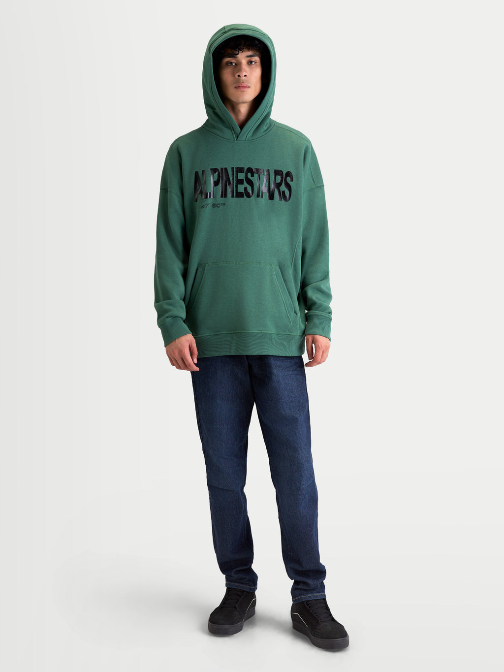 Alpinestars Shaw Oversized huvtröja, grön med svart texturerad logotyp, avslappnad passform för vardagsbruk, framifrån på modell, mjuk fleece i bomull och återvunnen polyester, känguruficka och ribbade avslut