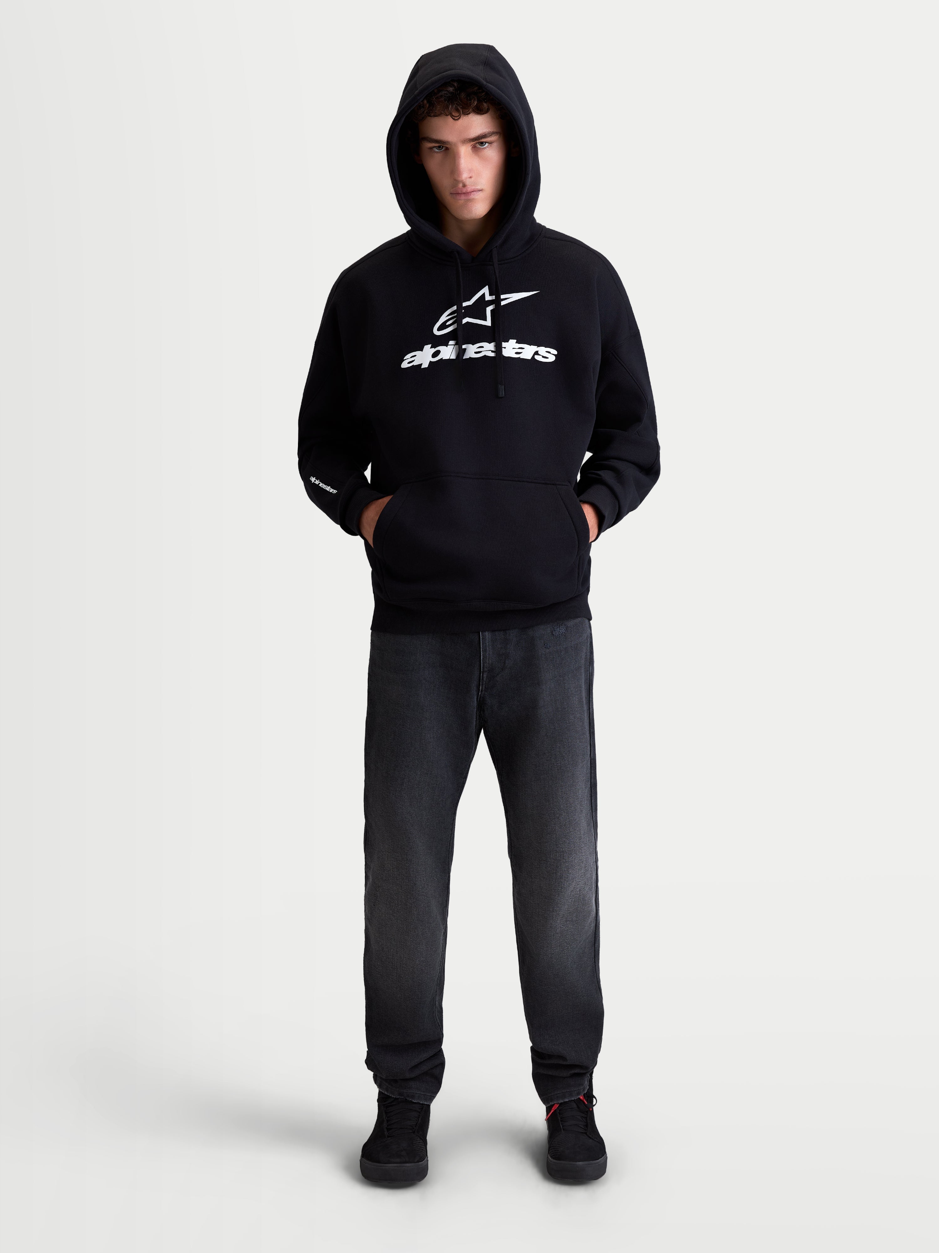 Alpinestars Prelude Oversized Hoodie, Sportswear Fleece Pullover, Unisex, Black and White, Cotton and Recycled Polyester, Relaxed Oversized Fit featuring a kangaroo pocket and bold puff-print logos on the chest and sleeve, shown on model.