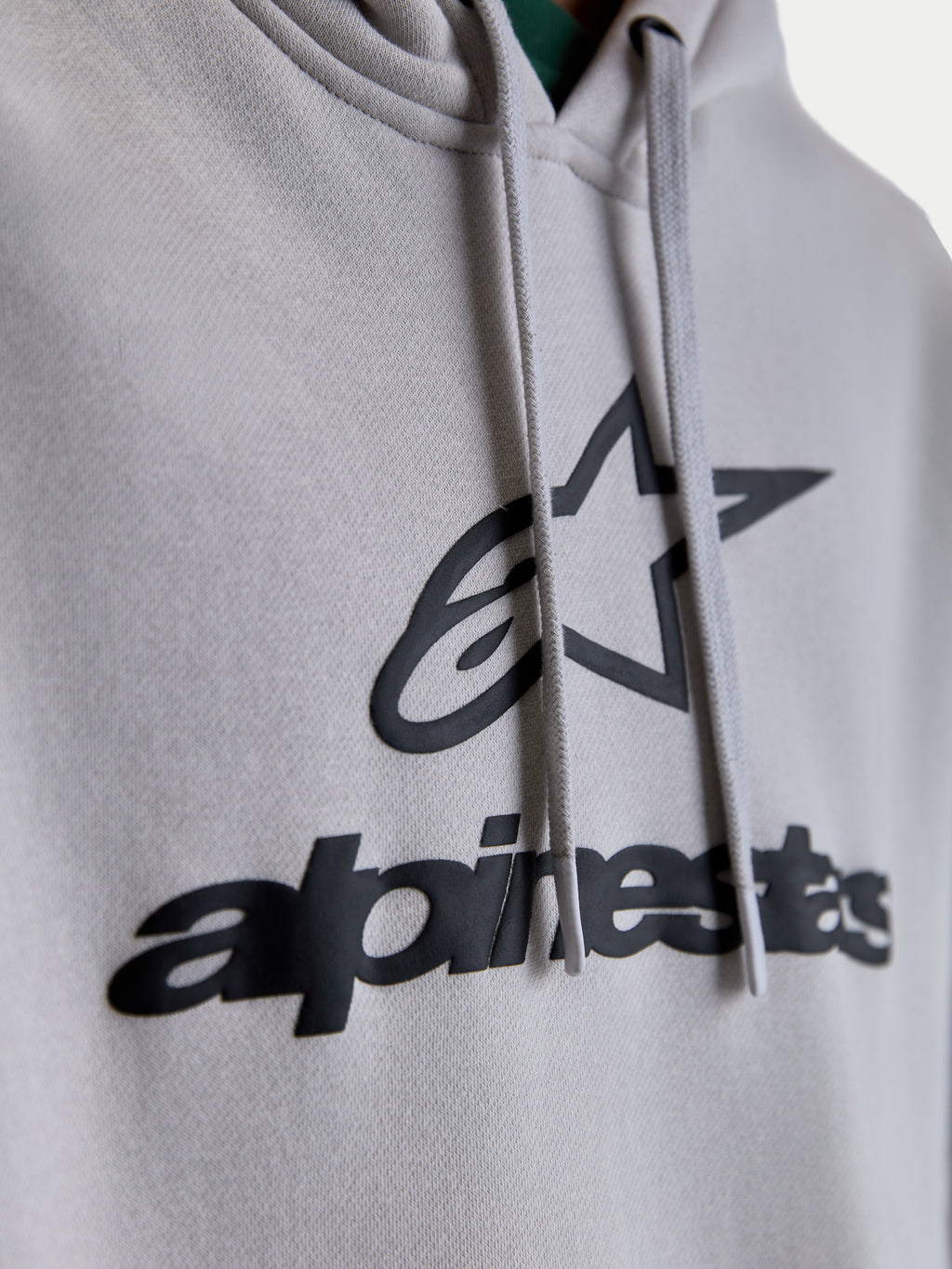Alpinestars Prelude Oversized huvtröja, närbild på svart pufftryckt logotyp och stjärngrafik på cementgrå fleece, platta dragskor, premium unisex sportswear