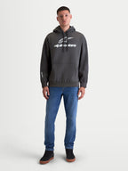 Alpinestars Prelude Oversized huvtröja, mörkgrå fleecehuvtröja i sportswear-stil, känguruficka och puff-printade logotyper på bröstet och ärmen, visas på modell för vardagsbruk.