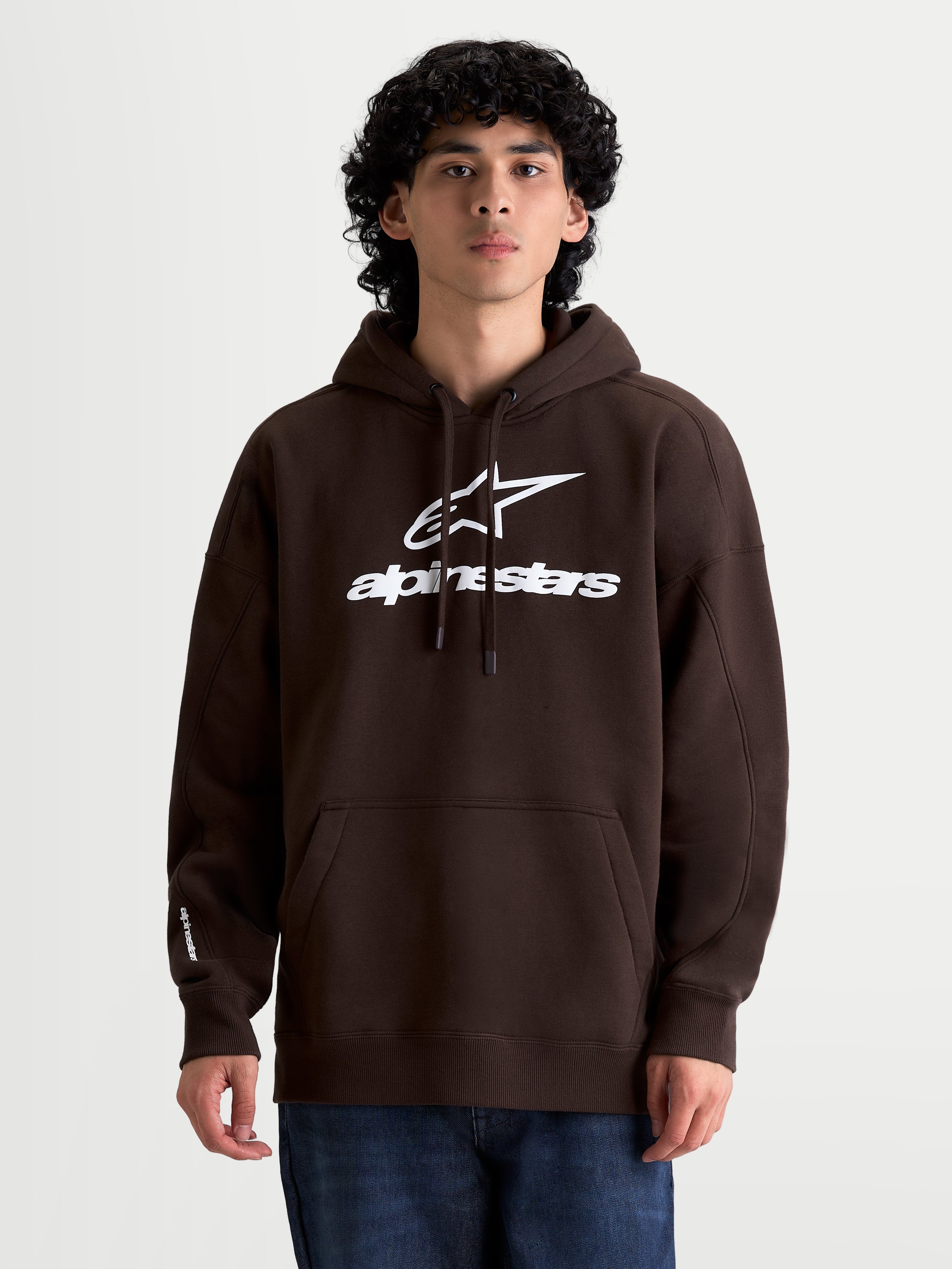 Alpinestars Prelude Oversized huvtröja på modell, brun huvtröja för herrar med vit puff-printad logotyp, avslappnad passform, känguruficka och huva med dragsko, mjuk bomullsfleece.