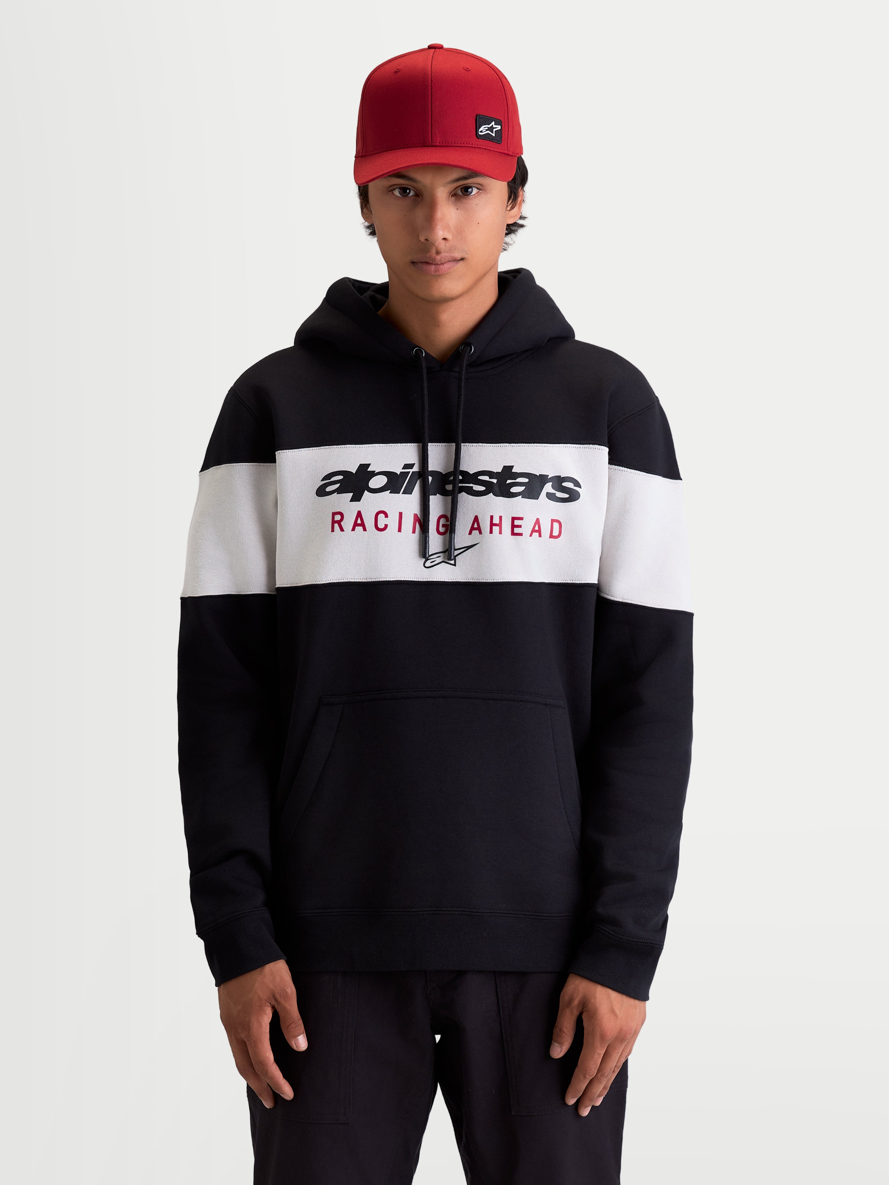 Alpinestars Cubic huvtröja på modell, sportswear-huvtröja för herrar i svart och vit färgblockerad fleece, Alpinestars Racing Ahead-logotyp på bröstet, huva med dragskor och känguruficka, bekväm livsstilsklädsel för fritidsbruk.