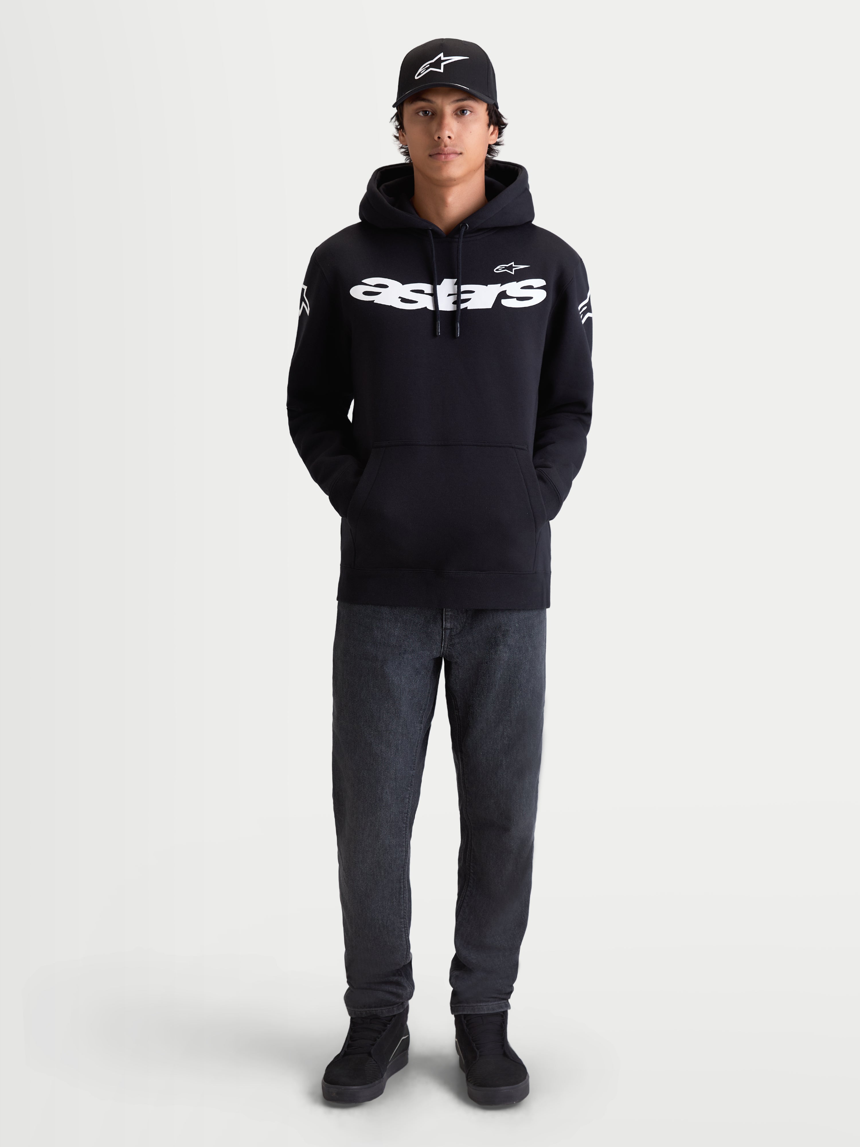 Alpinestars Velocifier huvtröja, svart pullover i fleece för herrar, vit Astars-logotyp på bröstet och axlarna, premium bomullsblandning, visas på modell med matchande keps för bekvämt vardagsbruk.