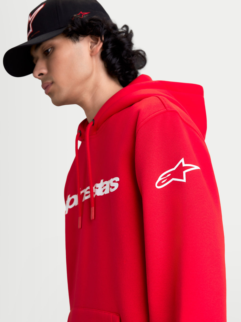 Alpinestars Race Wordmark huvtröja, röd och vit sporttröja i fleece, visas på modell med vit Ageless-logotyp på ärmen och Race Linear-branding framtill, avslappnad motorsport-inspirerad design