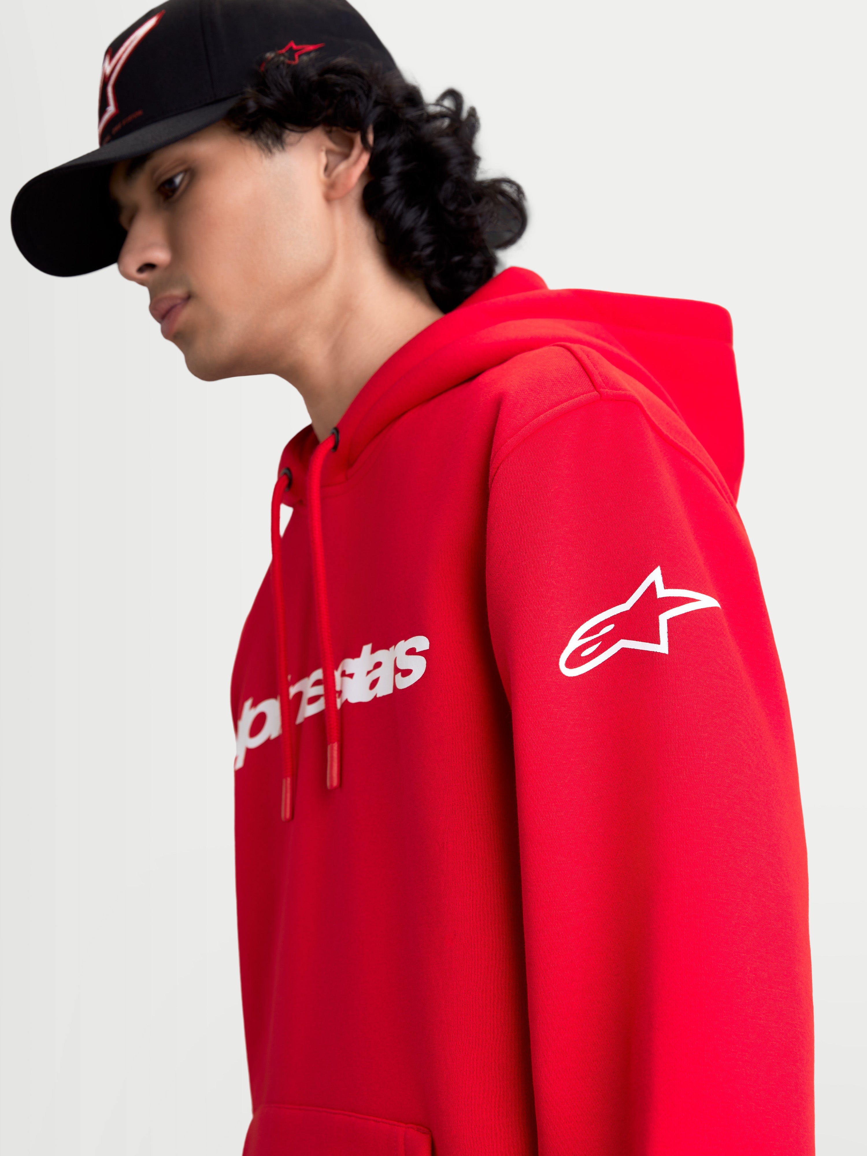 Alpinestars Race Wordmark huvtröja, röd och vit sporttröja i fleece, visas på modell med vit Ageless-logotyp på ärmen och Race Linear-branding framtill, avslappnad motorsport-inspirerad design