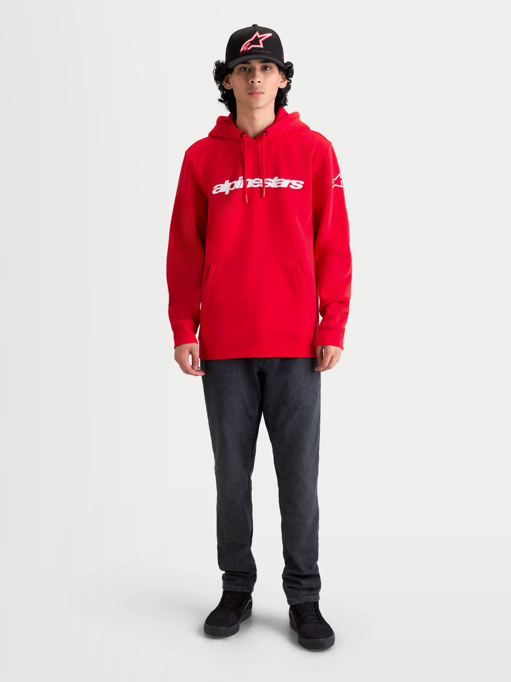 Alpinestars Race Wordmark huvtröja, röd och vit sportig huvtröja i fleece, motorsport-inspirerad look med känguruficka och justerbar dragsko, bärs av modell för en avslappnad stil.