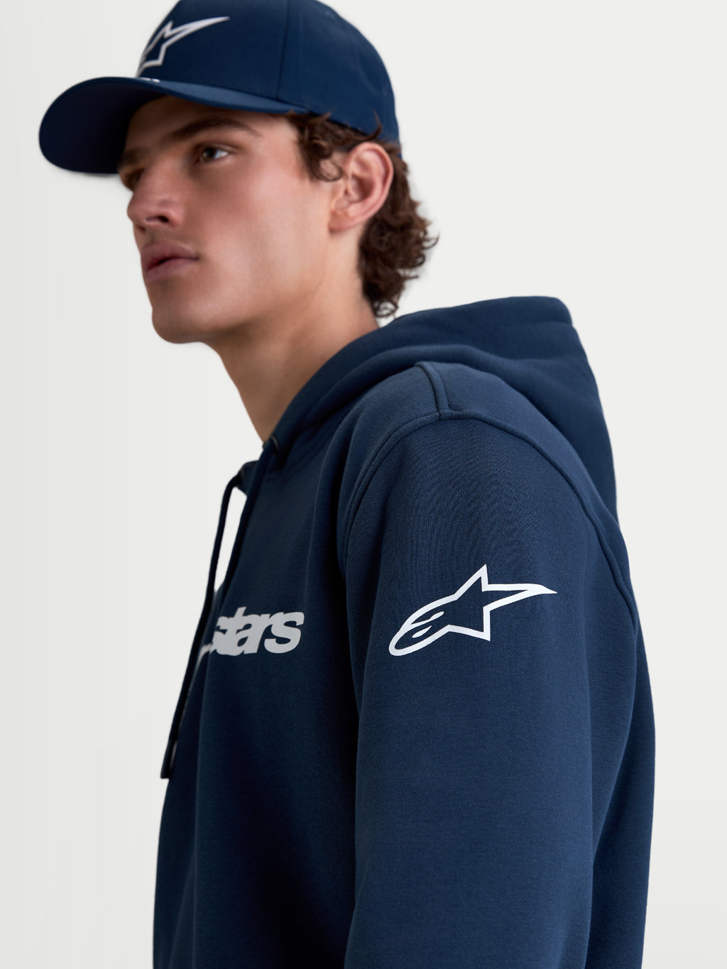 Alpinestars Race Wordmark huvtröja, sportig huvtröja i fleece för herrar, mörkblå och vit, med Ageless-logotyp på ärmen och Race Wordmark på bröstet, livsstilsbild på modell.