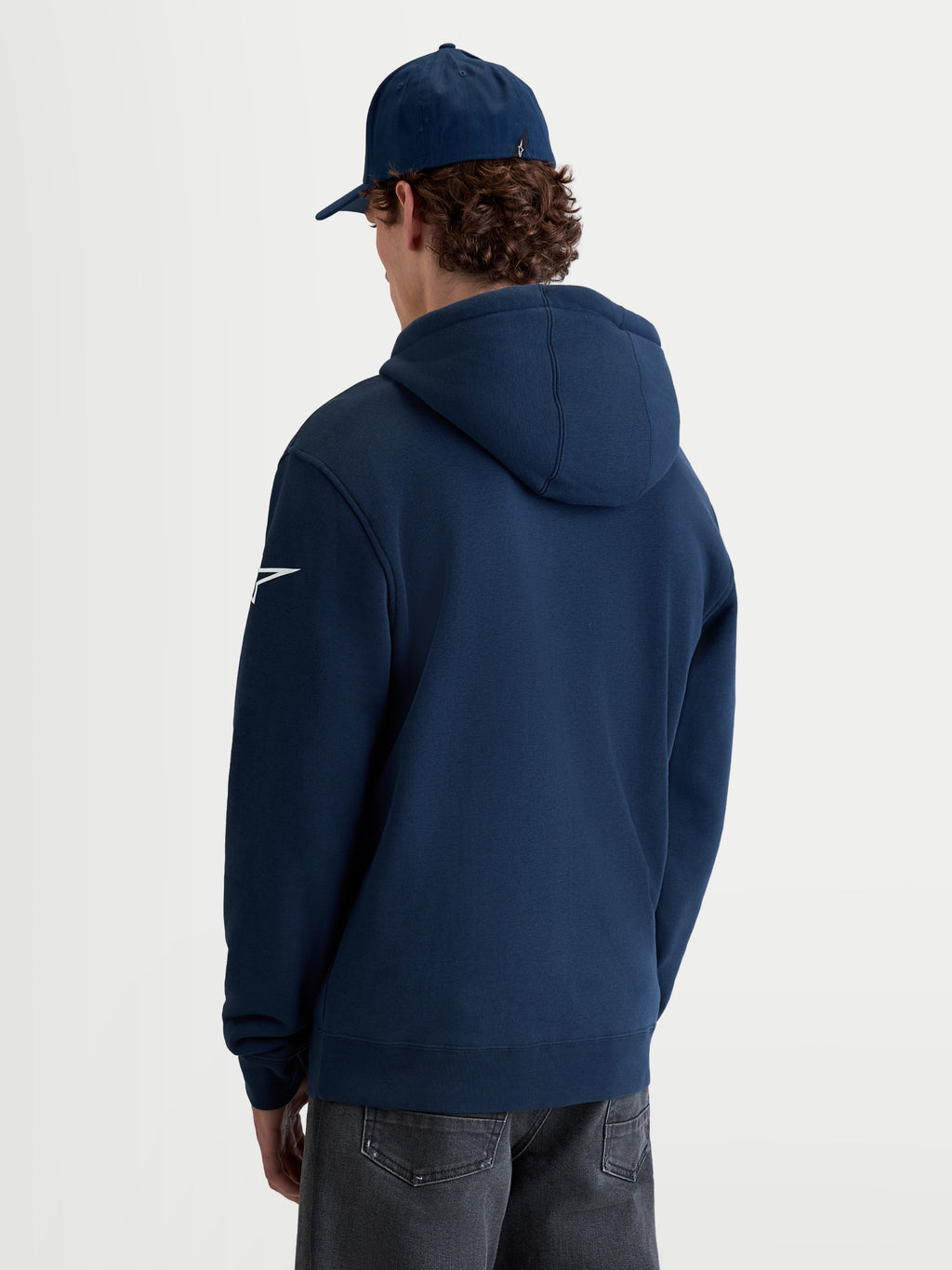 Alpinestars Race Wordmark huvtröja, marinblå herrhuvtröja i pullover-fleece, vy bakifrån på modell med vit Ageless-logotyp på ärmen och självfodrad huva, bekväma sportkläder inspirerade av motorsport