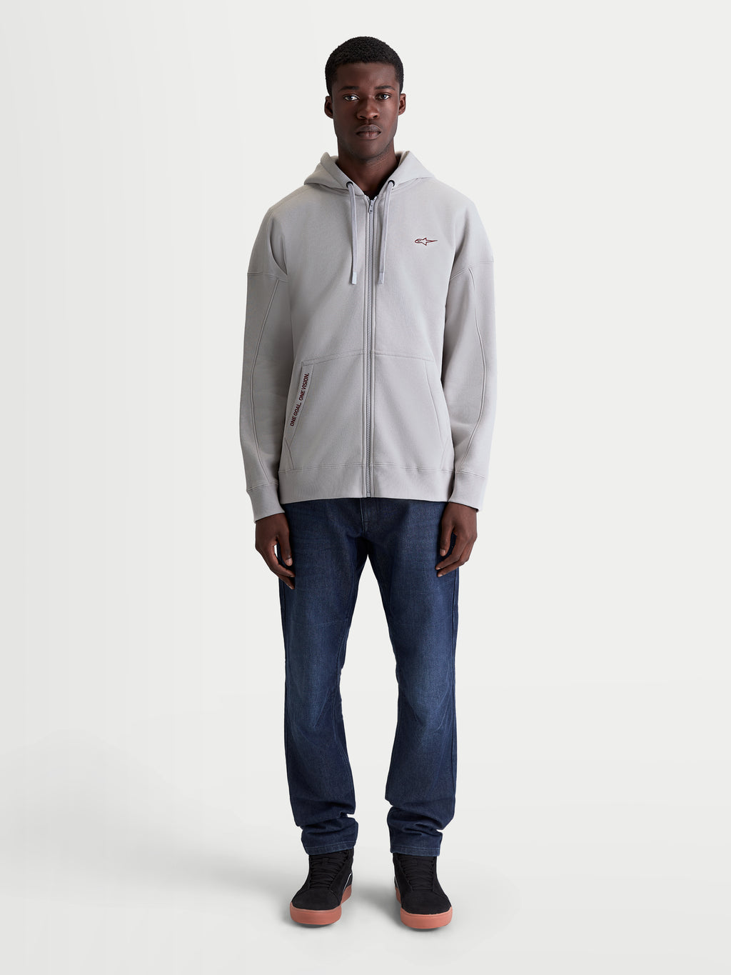 Alpinestars Pioneer Oversized huvtröja, grå sportig fleecehoodie med dragkedja, oversizepassform, Vislon-dragkedja och känguruficka, broderad One Goal One Vision-branding, helkroppsbild framifrån på modell.