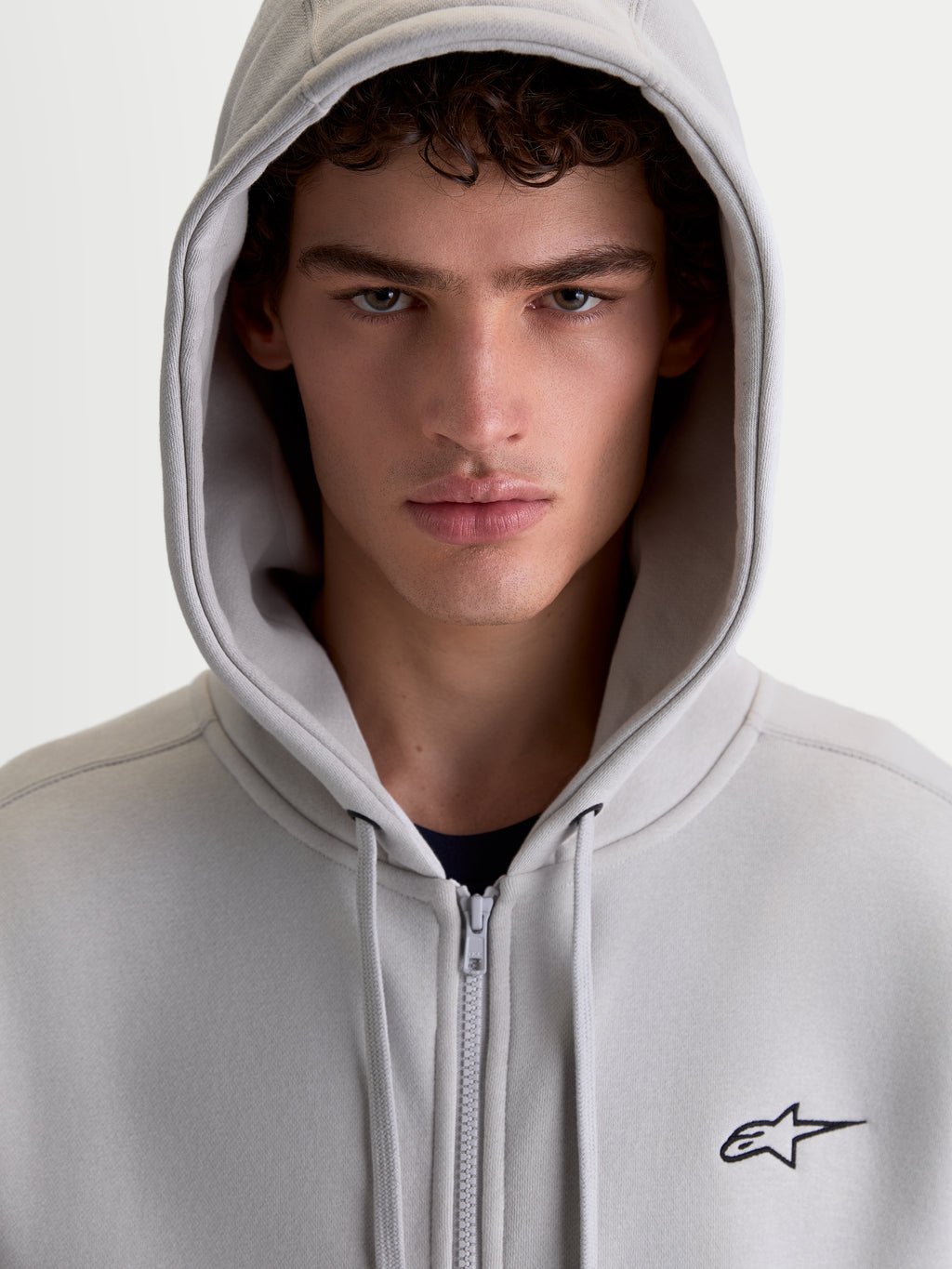 Alpinestars Entity Oversized huvtröja, cementgrå fleecehuvtröja med dragkedja för herr och dam, broderad Astars-logga och Vislon-dragkedja, närbild på modell med huvan uppe.