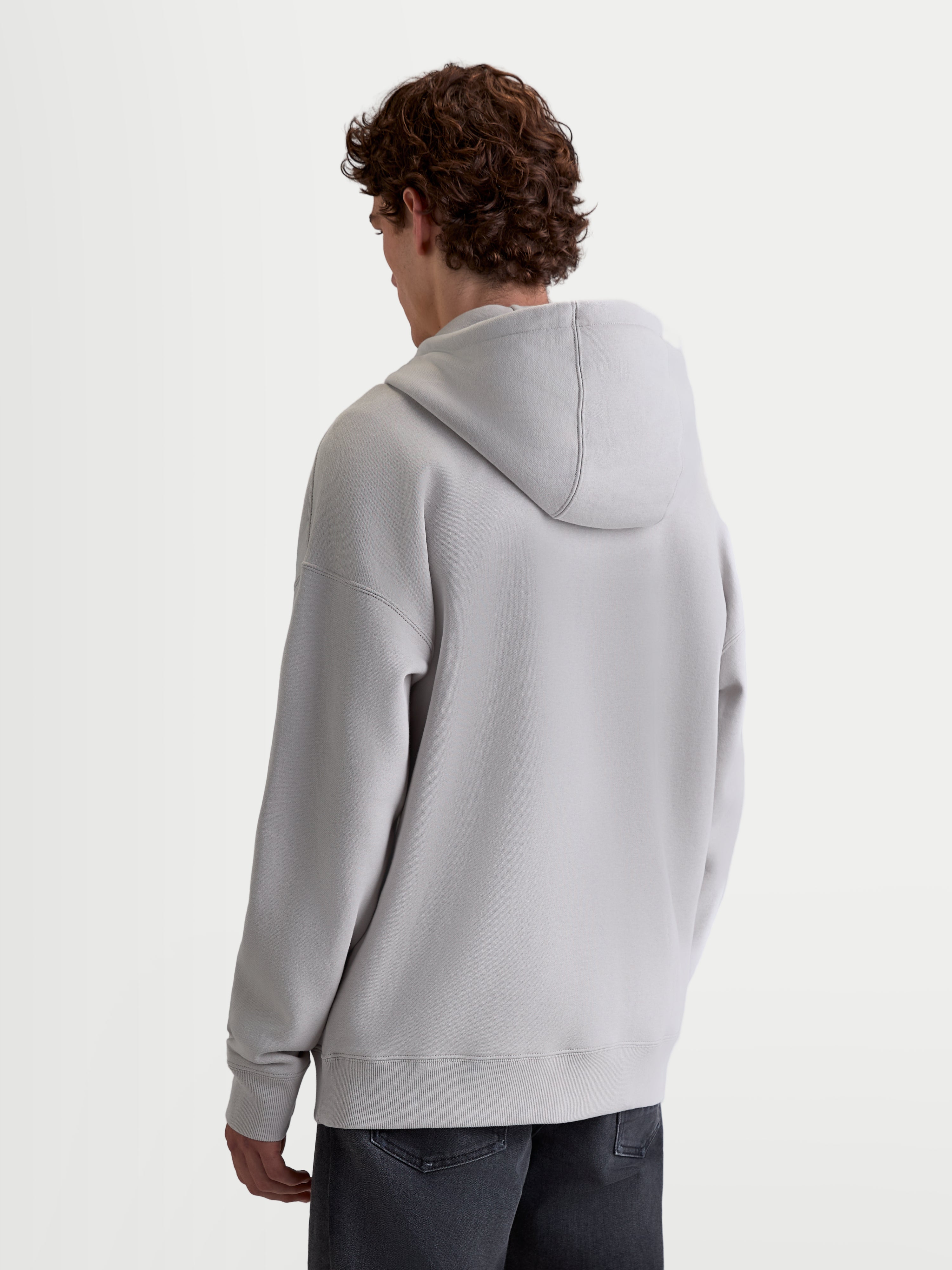 Alpinestars Entity Oversized huvtröja, ledig fleecehuvtröja för herr och dam, sedd bakifrån på modell, grå, avslappnad passform med sänkta axlar, fodrad huva och ribbade muddar.