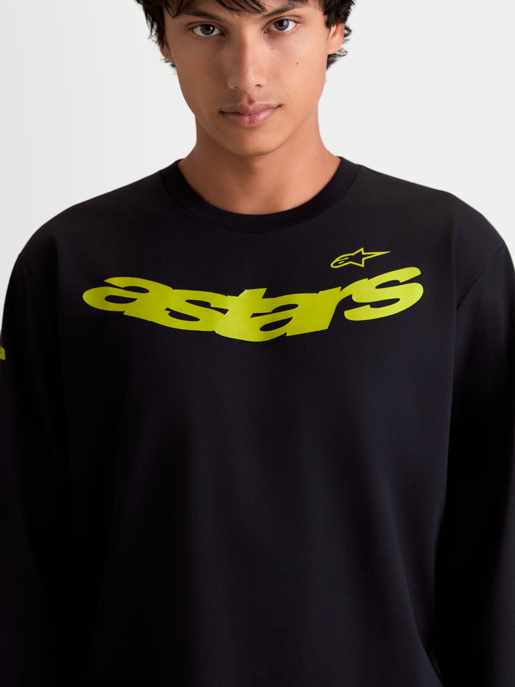 Alpinestars Velocifier CSF långärmad t-shirt på modell, svart med gul böjd astars-logotyp på bröstet, mjuk bomullsblandning, motorsportinspirerad sportswear.