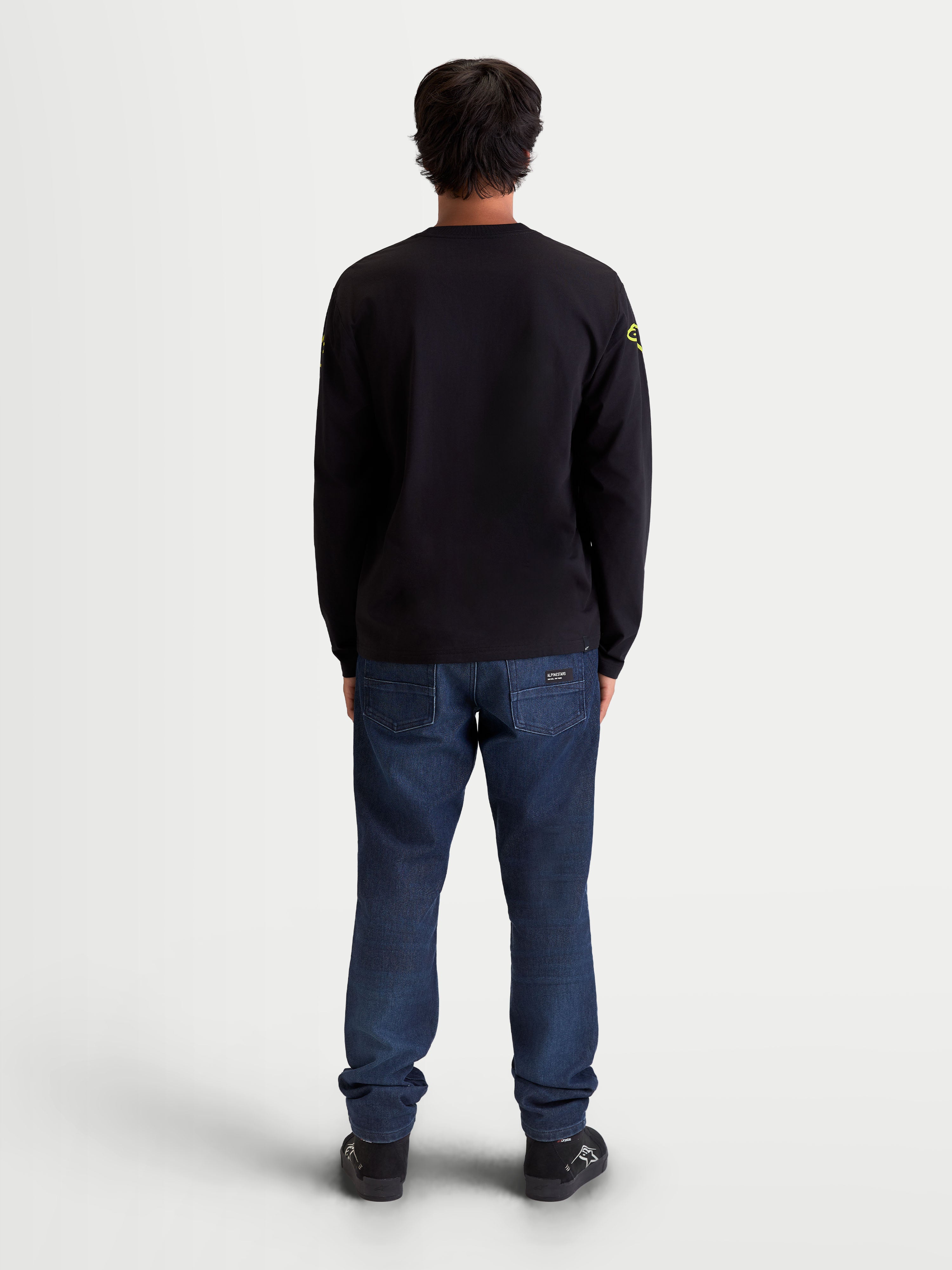 Alpinestars Velocifier CSF långärmad t-shirt, svart med gula axellogotyper, sedd bakifrån på modell, motorsport-inspirerad sportswear i bomull och återvunnen polyester med ribbade muddar.