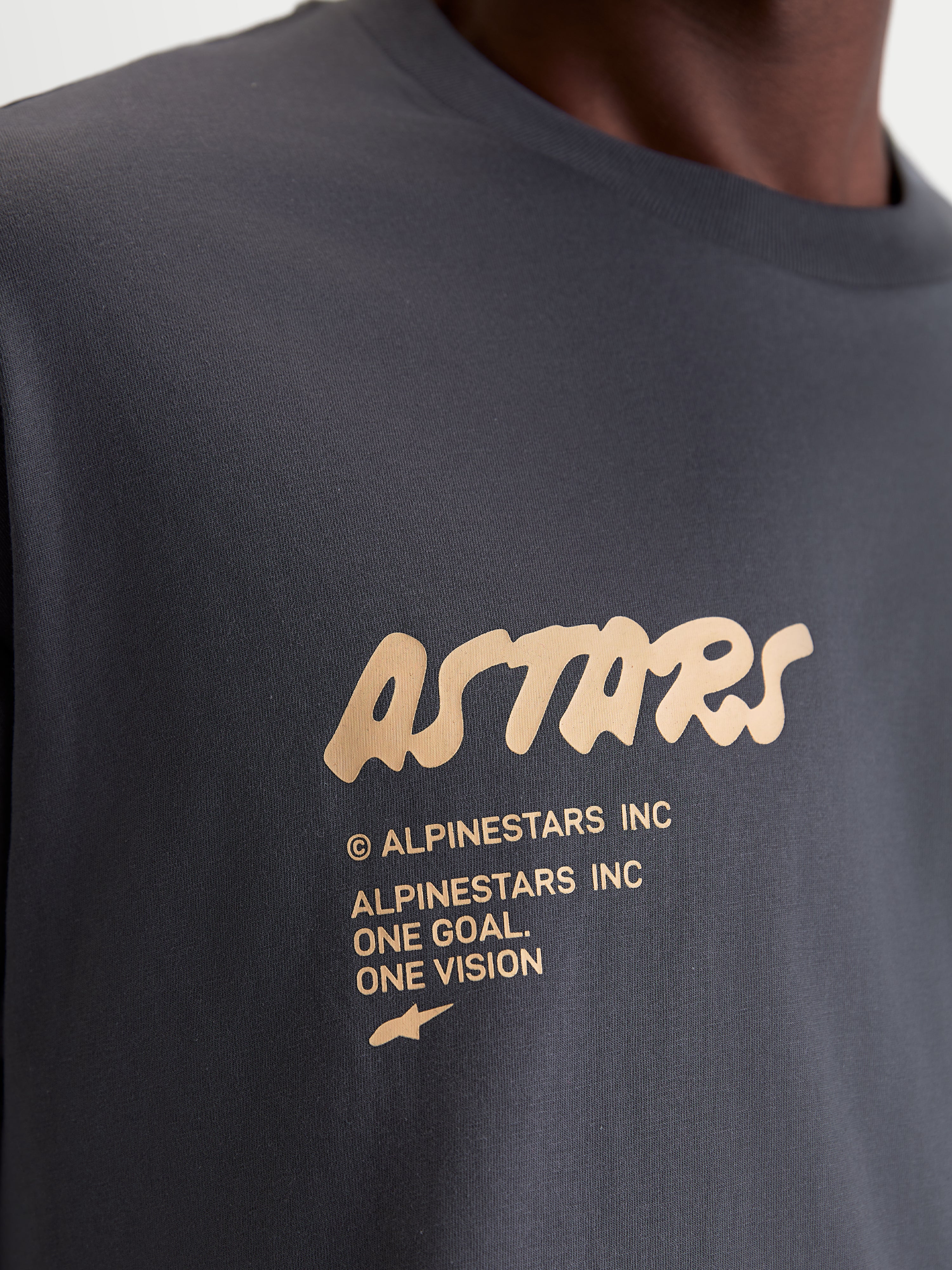 Alpinestars Chalk Oversized CSF T-shirt, mörkgrå kortärmad sportswear-T-shirt, närbild på beige Astars-ordmärke och One Goal One Vision-branding på bröstet, avslappnad motorsportinspirerad stil