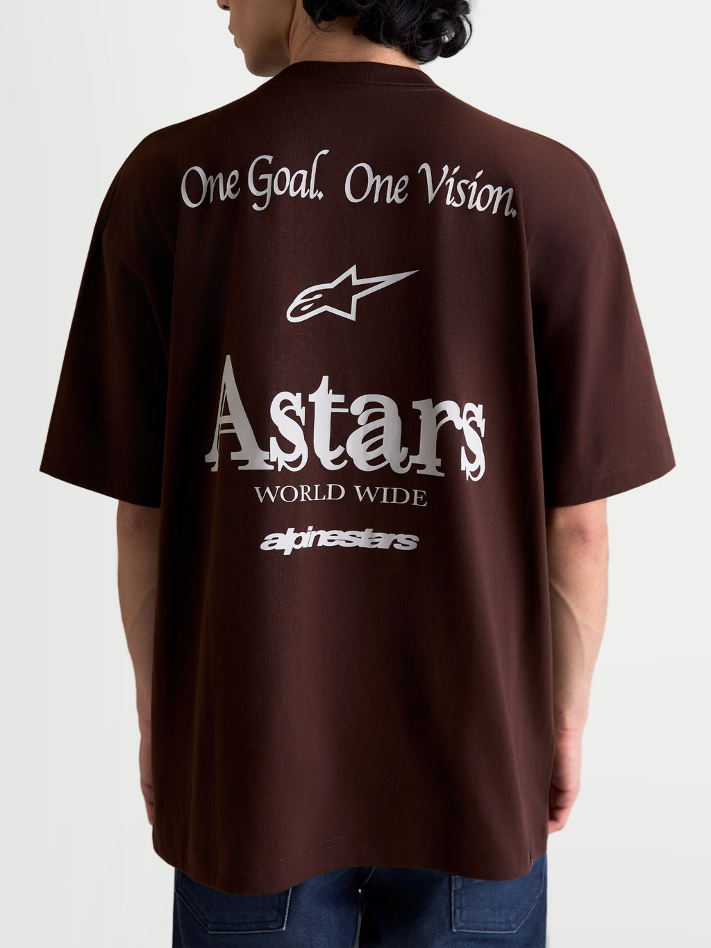 Alpinestars Post Oversized CSF t-shirt, brun kortärmad t-shirt i sportswear-stil, bakifrån på modell med vit grafik 'One Goal. One Vision.' och 'Astars World Wide', avslappnad passform i mjuk bomullsblandning.