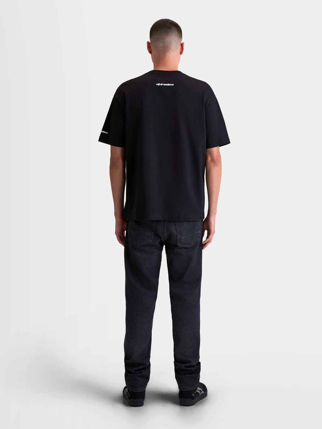 Alpinestars Mandate Oversized CSF Tee, Men's Sportswear Short Sleeve T-Shirt, Black with white graphics, back view showing relaxed oversized fit and small wordmark branding on the neck and sleeve, 60/40 cotton-poly blend.