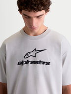 Alpinestars Prelude Oversized CSF t-shirt, kortärmad sporttröja i cementgrå med svart logotypgrafik på bröstet, oversized passform, mjuk bomull-polyesterblandning, lifestyle-topp visad på modell
