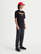 Alpinestars Elliptogrit CSF t-shirt på modell, kortärmad svart sportswear t-shirt för herrar med gul och röd gradient Astars-logotyp och vit grafisk logotyp på bröstet, bekväm bomullsblandning för vardagsbruk.