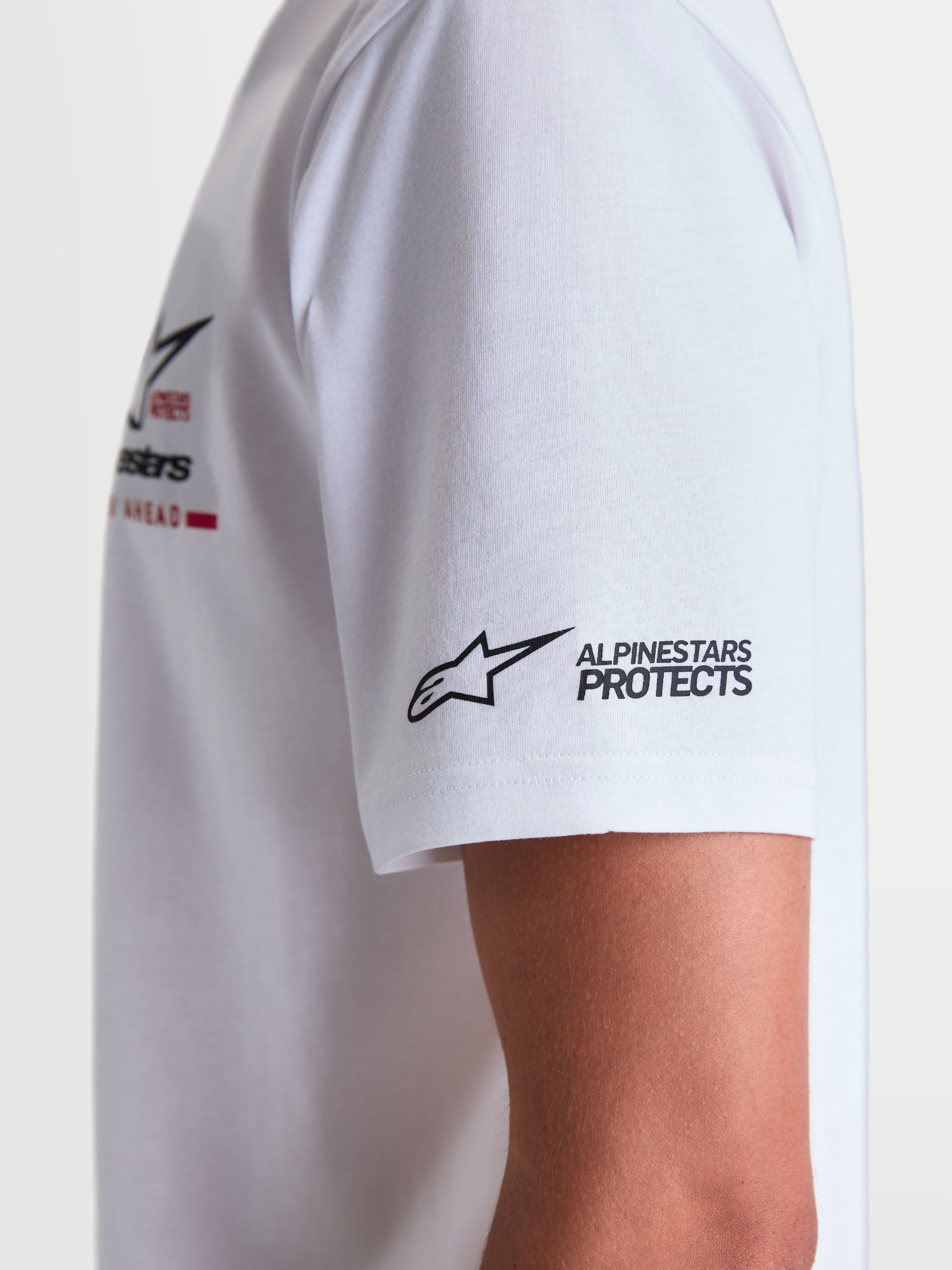 Alpinestars P1 CSF t-shirt, vit kortärmad t-shirt i mjuk bomull-polyesterblandning, närbild på ärm med svart Alpinestars Protects-logotyp och detalj av racingrandig grafik på bröstet, casual sportswear för herrar och damer