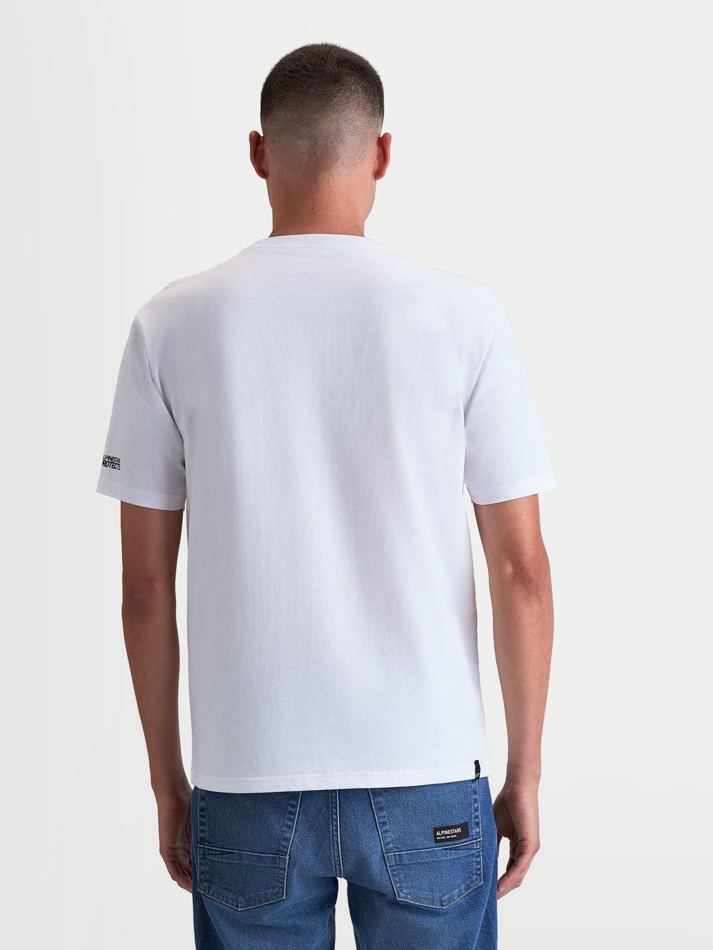 Alpinestars P1 CSF t-shirt, vit kortärmad t-shirt för herrar, sedd bakifrån på modell, avslappnad motorsport-streetwear i mjuk bomullsblandning