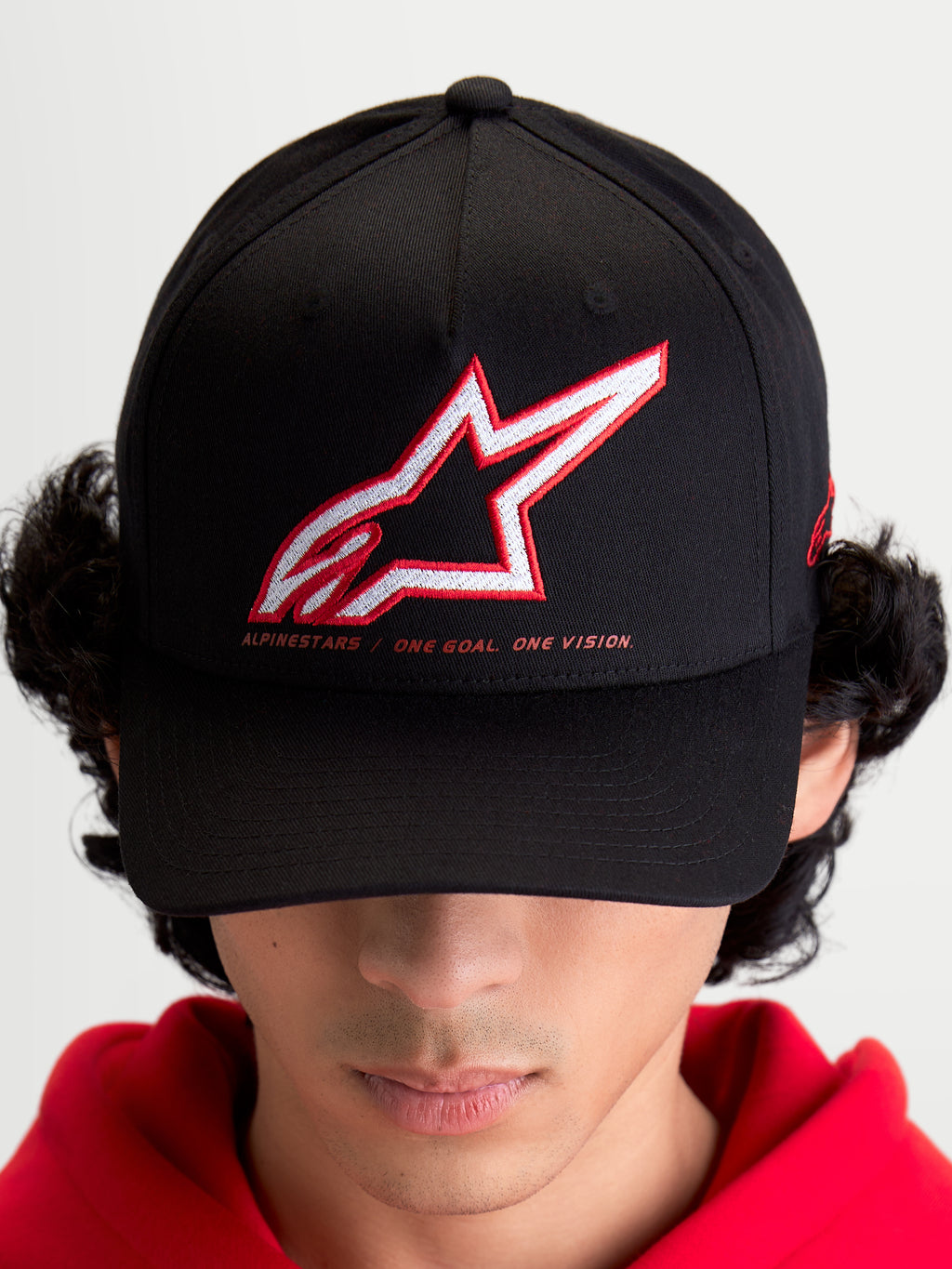 Alpinestars Lineout keps på modell, sportswear baseballkeps för herrar och damer, svart med röd och vit broderad Astars-logotyp och sloganen One Goal One Vision, böjd skärm, strukturerad krona